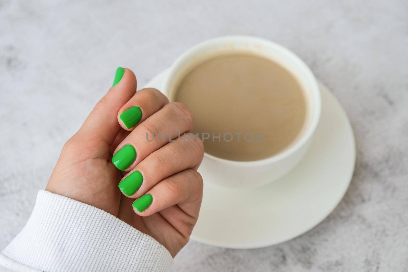 Manicured female hands with stylish green nails holding cup of coffee. Take a break for coffee latte. Trendy modern design manicure. Gel nails. Skin care. Beauty. Nail care. Wellness