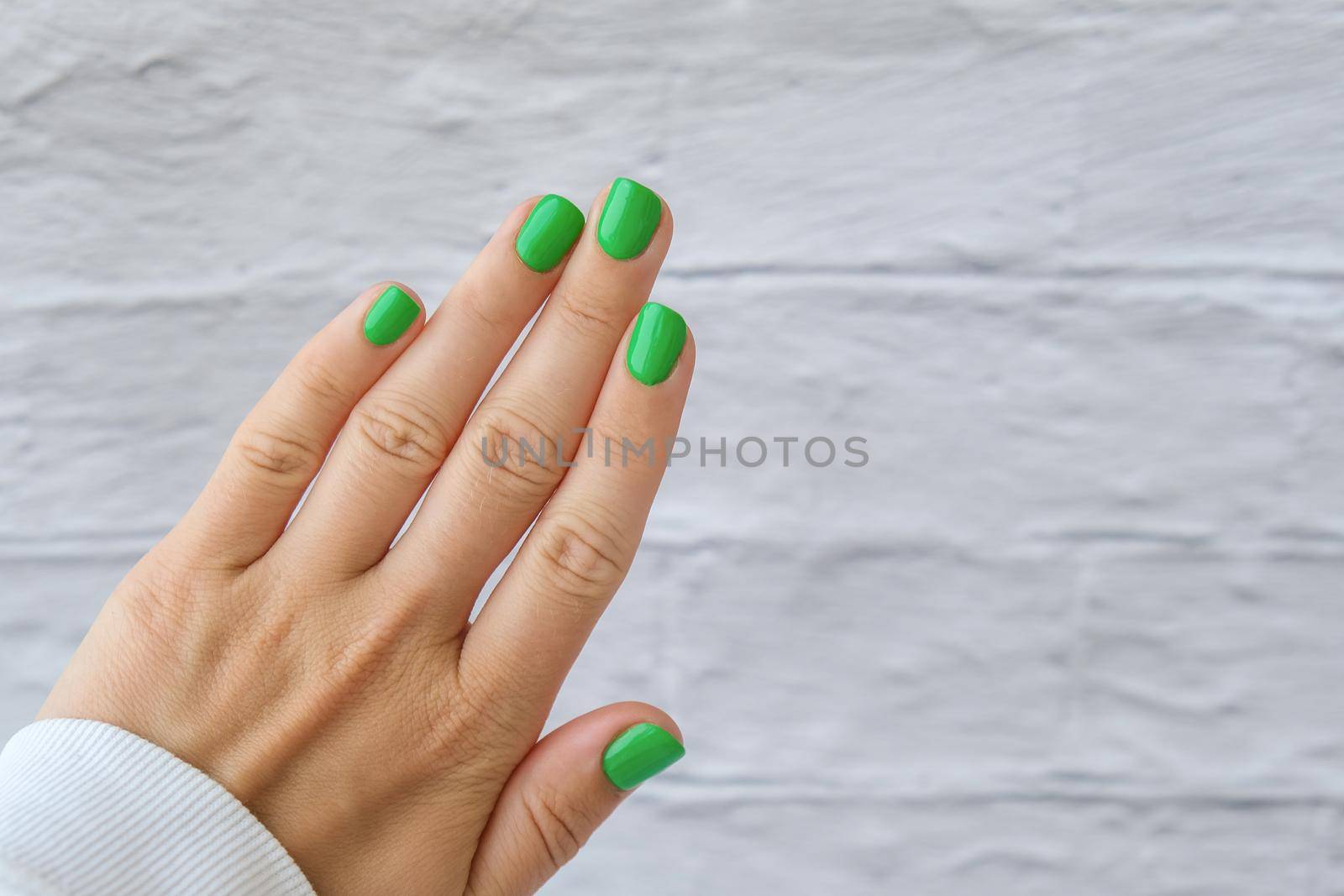 Manicured female hands with stylish green nails. Trendy modern design manicure. Gel nails. Skin care. Beauty treatment. Nail care. Wellness. Trendy colors.