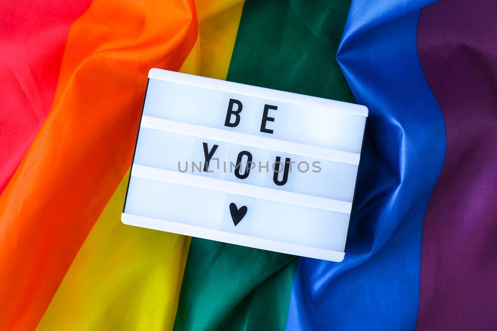 Rainbow flag with lightbox and text BE YOU. Rainbow lgbtq flag made from silk material. Symbol of LGBTQ pride month. Equal rights. Peace and freedom. Support LGBTQ community