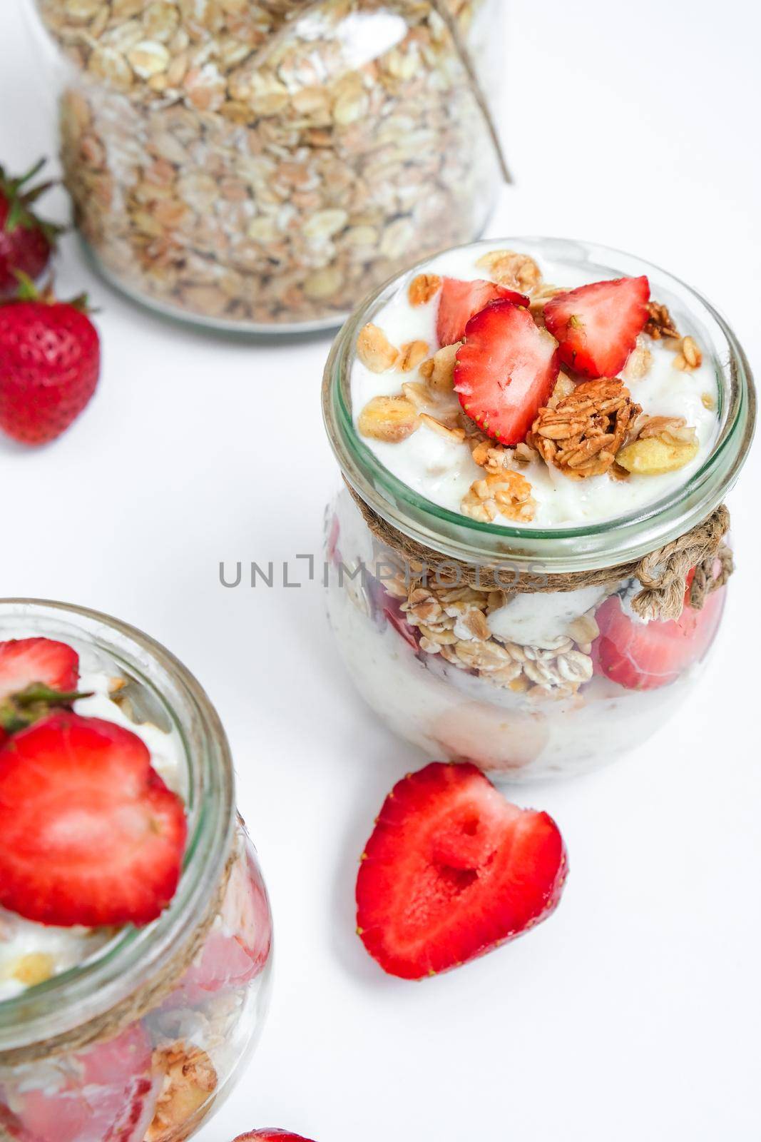 Healthy breakfast. Oatmeal Granola with greek yogurt and nuts strawberry muesli in jars on light background. Vegan, vegetarian and weight loss diet concept. Detox menu. by anna_stasiia