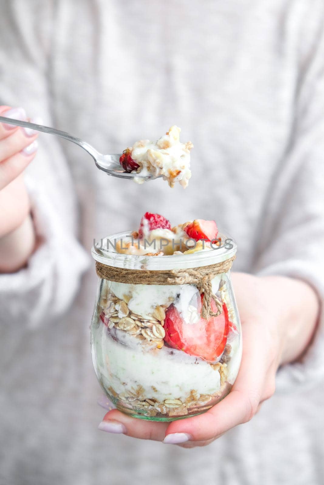 Female hands woman eating Healthy breakfast. Oatmeal Granola with greek yogurt and nuts strawberry muesli in jars on light background. Fitness. Weight loss diet concept. Detox menu. by anna_stasiia