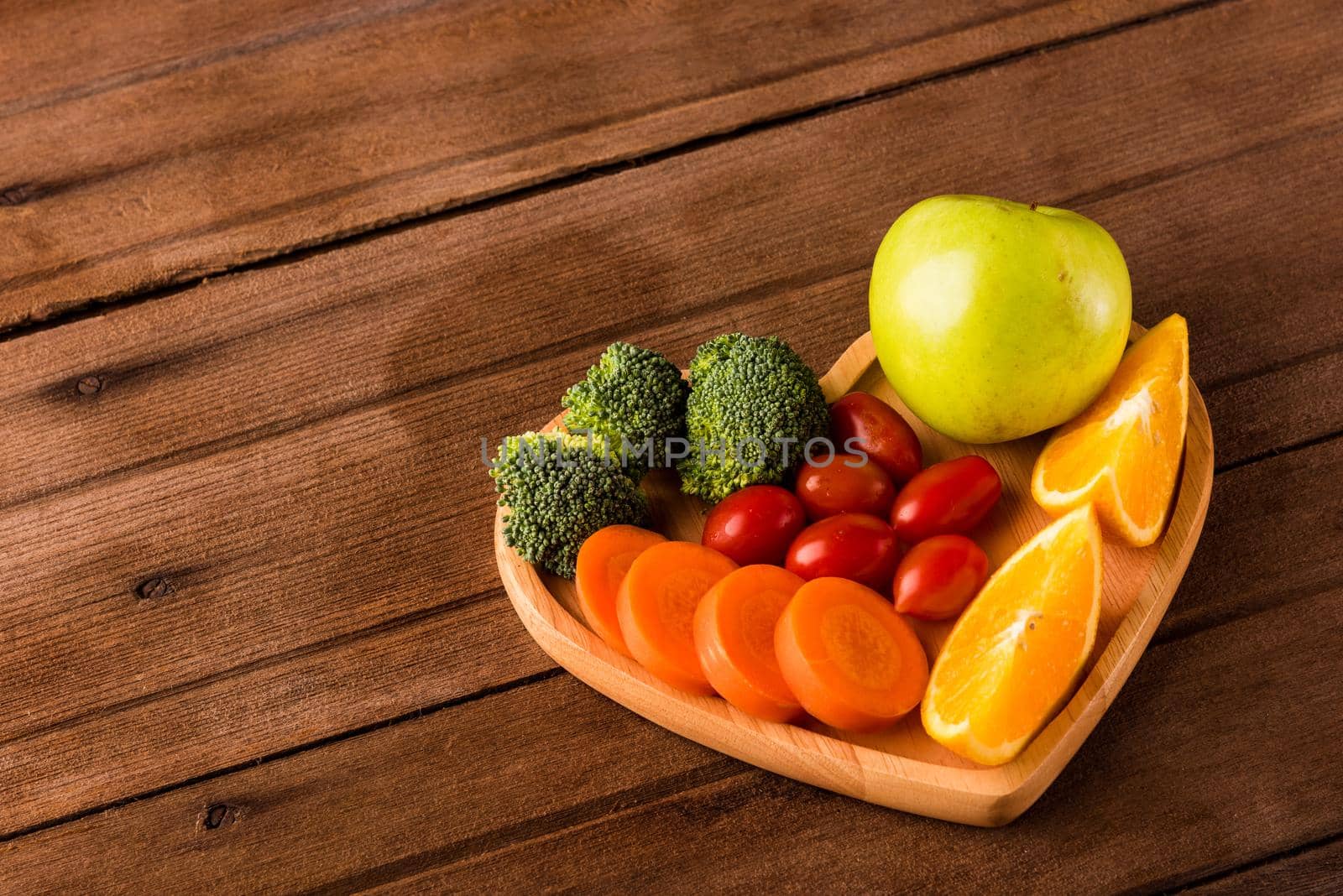 Top view of fresh organic fruits and vegetables in heart plate wood (apple, carrot, tomato, orange, broccoli) on wooden table, Healthy lifestyle diet food concept
