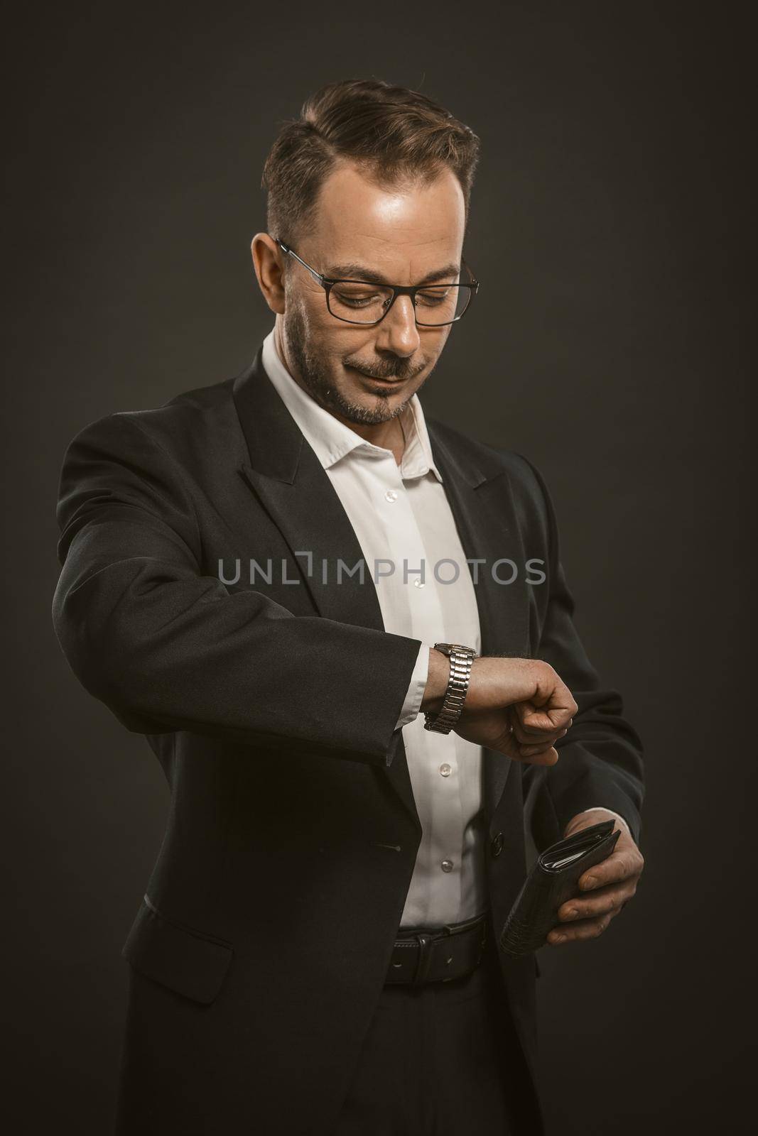 Businessman checks time looking at wristwatch. Friendly middle-aged man holds a purse in his hand while waiting for business meeting. Appointment concept. Toned image.