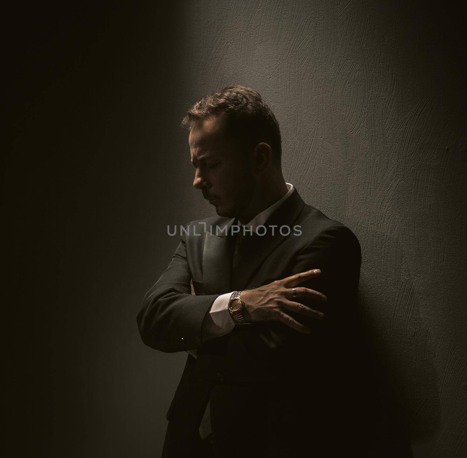 Pensive businessman stands against dark background. Thinking middle-aged man thoughtfully hugged himself with his hands against the wall. depression concept. bankruptcy concept. Toned image.