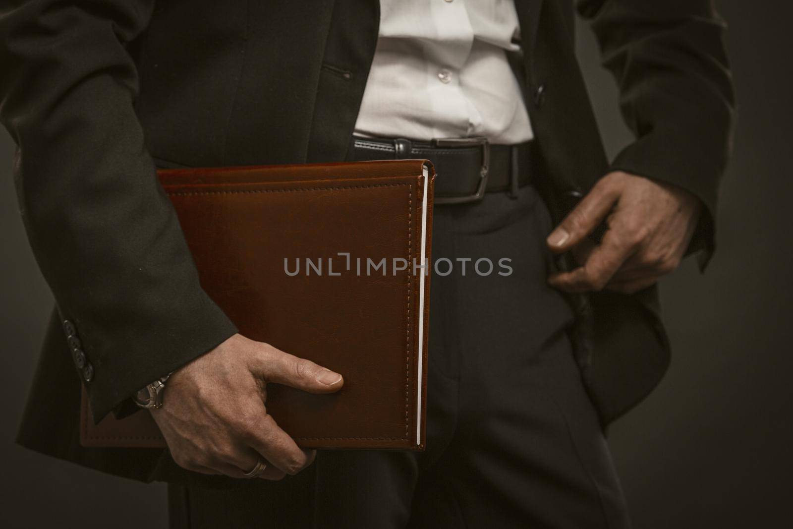 Successful businessman holds documents folder. Good looking caucasian man in formal wear holding brown leather document folder. Close up shot. Paperwork concept. Toned image.
