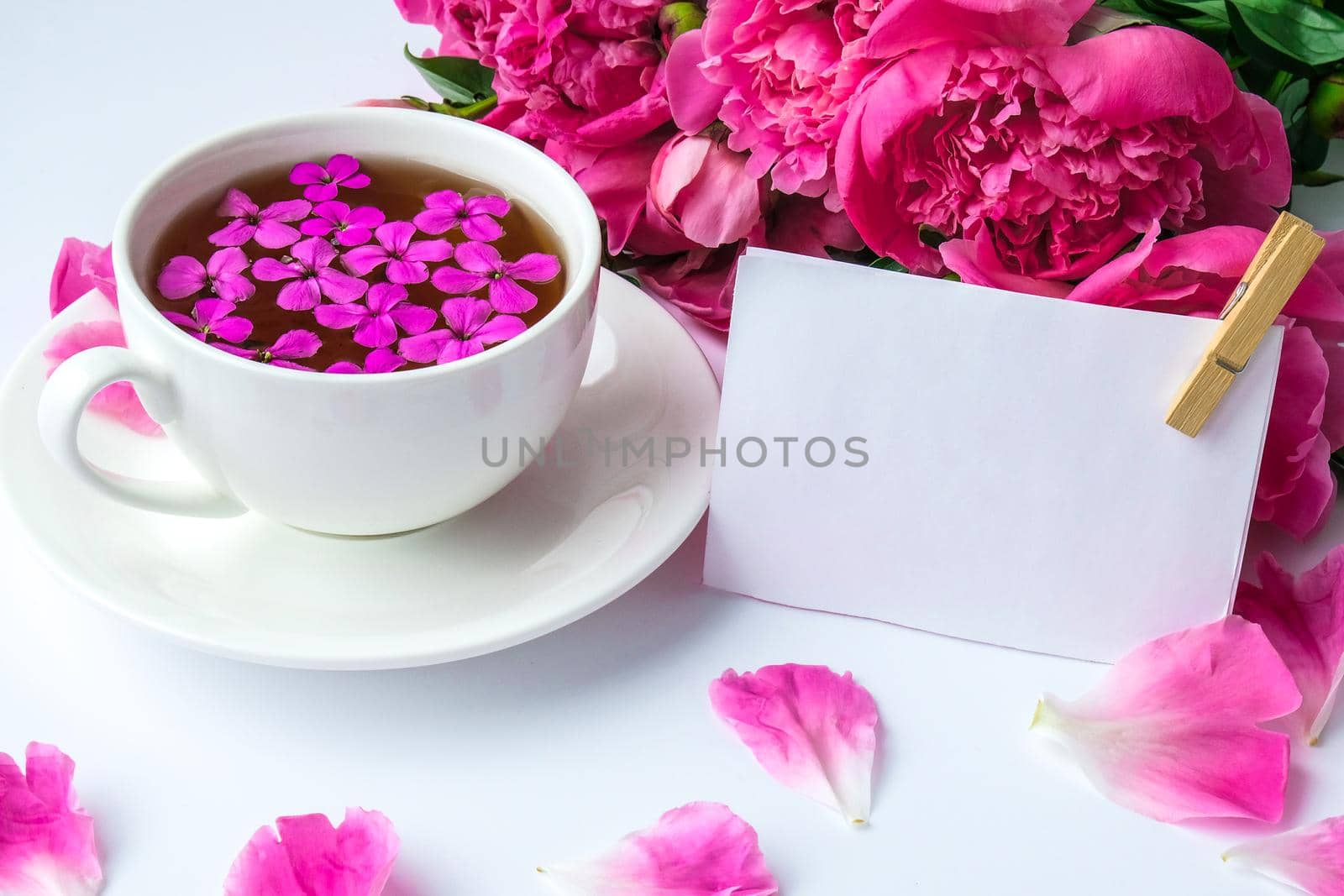 Creative layout with pink peonies flowers and cup of tea on bright table. Paper note. Copy space. Spring Seasonal valentine, woman, mother, 8 march holiday, romance breakfast. Stylish blogger. Greeting card. Invitation. Blog post