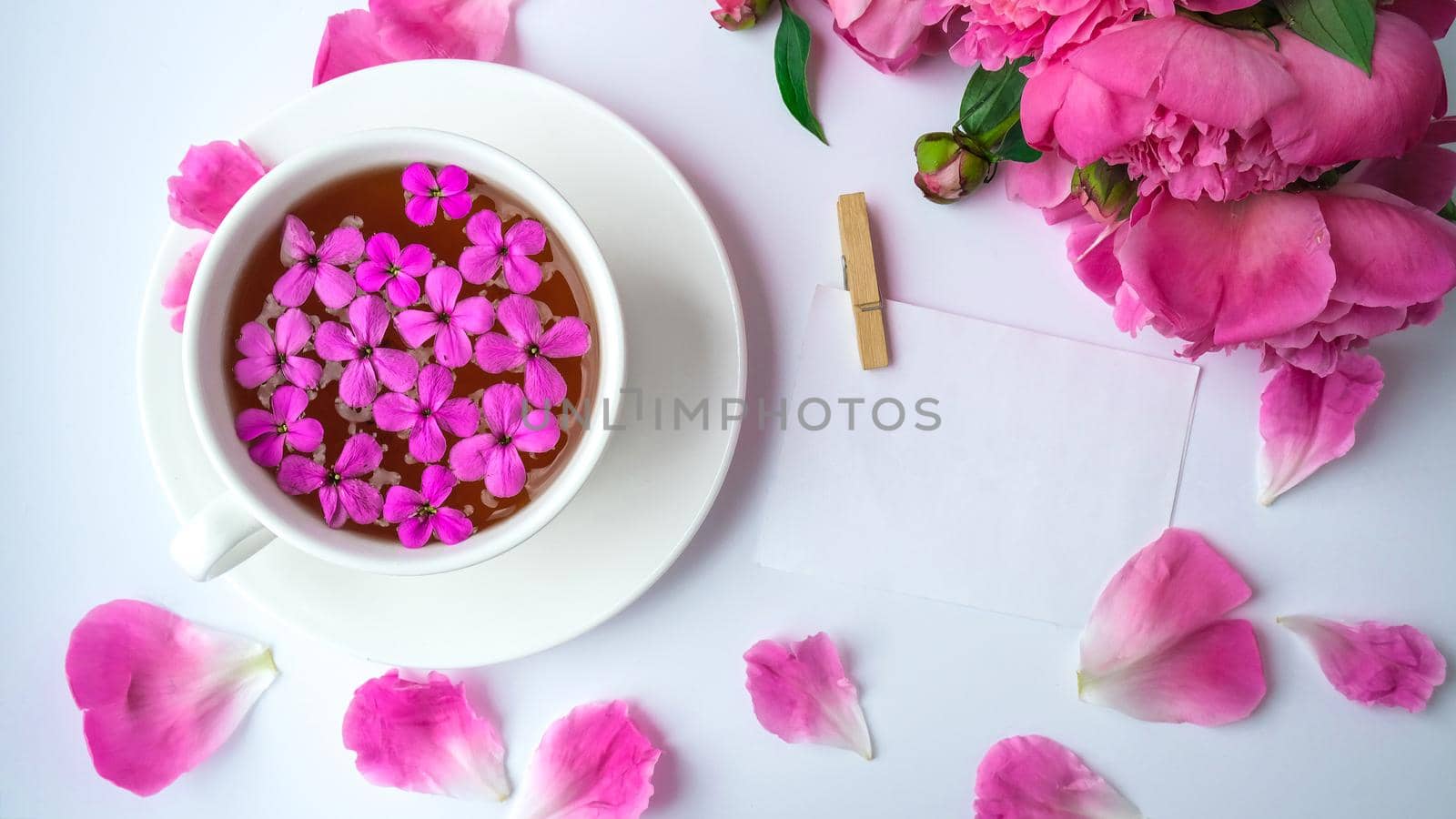 Creative layout with pink peonies flowers and cup of tea on bright table. Paper note. Copy space. Spring Seasonal valentine, woman, mother, 8 march holiday, romance breakfast. Stylish blogger. Greeting card. Invitation. Blog post