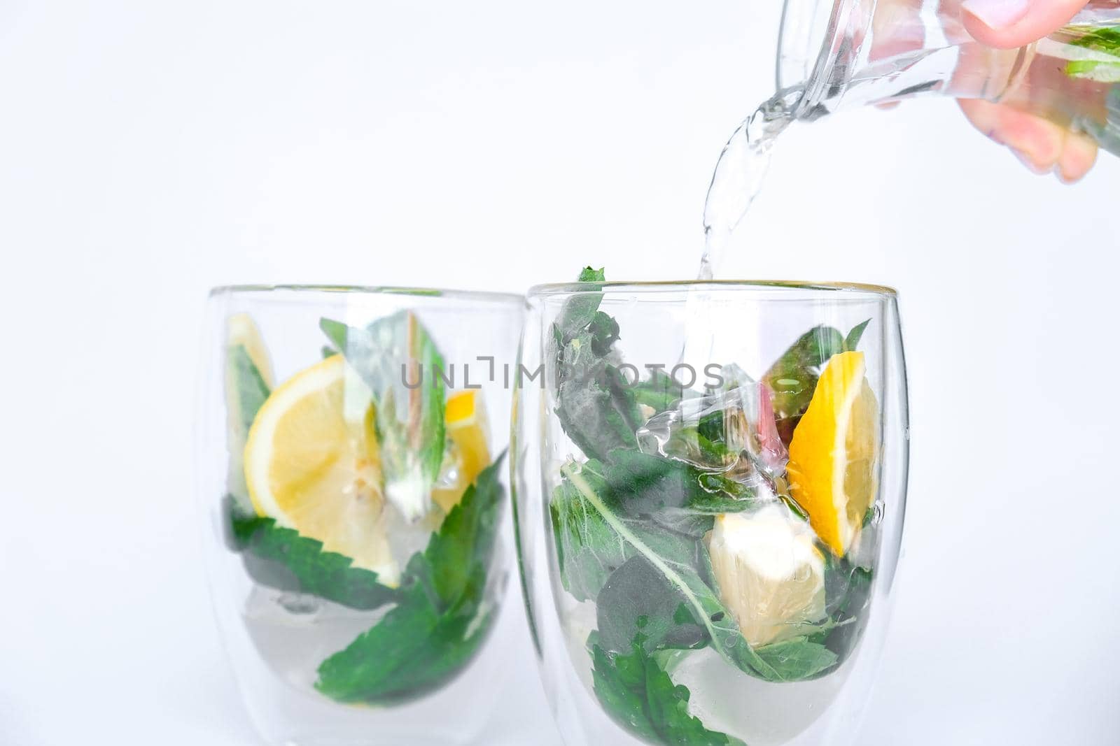Mojito refreshing cocktail pouring, alcohol drink. Lemonade with lemon and mint leaves on light background. Ice cubes. Summer refreshing detox drinks. Clean eating, healthy lifestyle concept, Diet. Nutrition.