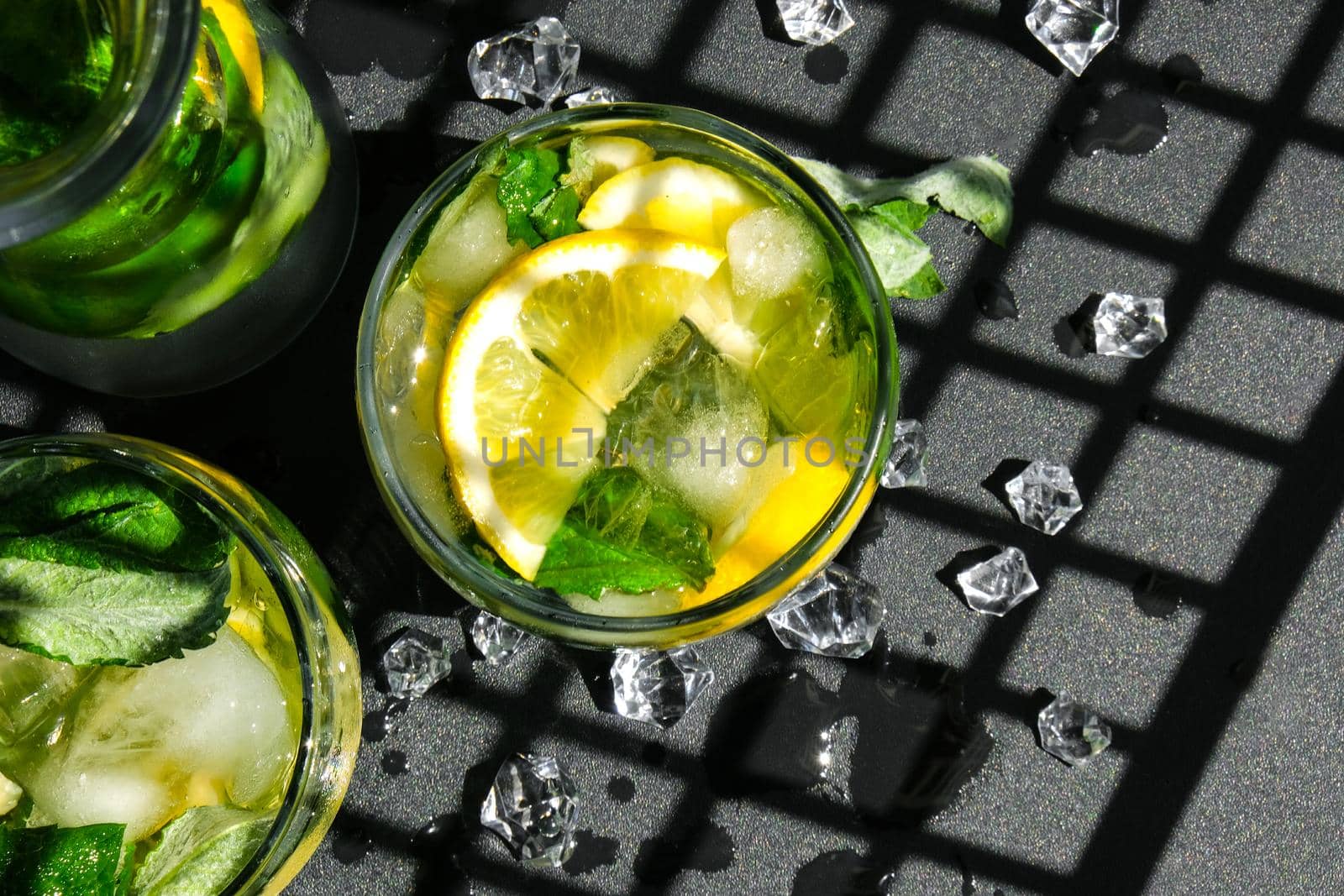 Mojito refreshing cocktail, alcohol drink. Lemonade with lemon and mint leaves on dark background. Trendy shadows Ice cubes. Summer refreshing detox drinks. Clean eating, healthy lifestyle concept, Diet. Nutrition. Top view