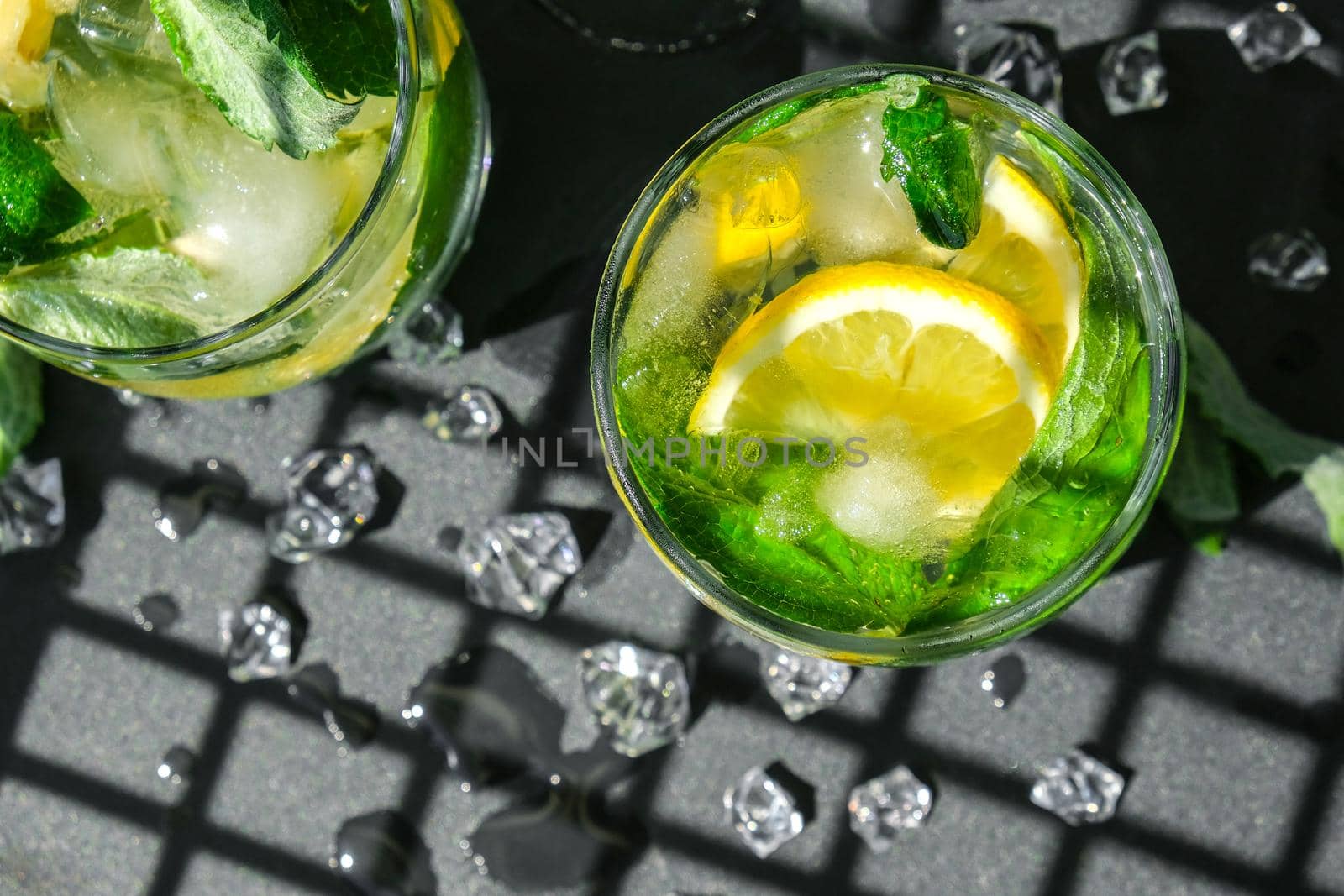 Mojito refreshing cocktail, alcohol drink. Lemonade with lemon and mint leaves on dark background. Trendy shadows Ice cubes. Summer refreshing detox drinks. Clean eating, healthy lifestyle concept, Diet. Nutrition. Top view