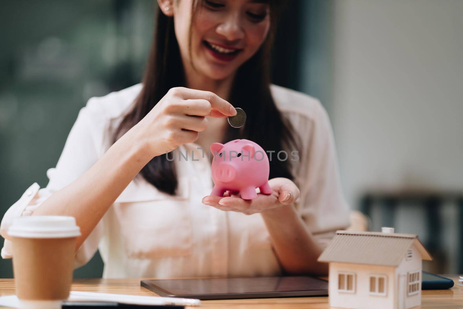 mortgage, investment, real estate and property concept - close up of woman putting money into pink piggy bank for loan or save for buy a new house by nateemee