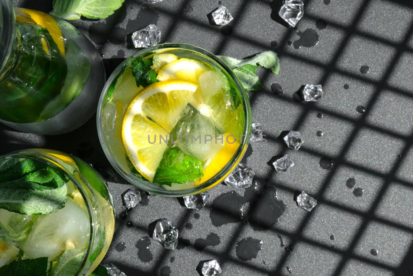 Mojito refreshing cocktail, alcohol drink. Lemonade with lemon and mint leaves on dark background. Trendy shadows Ice cubes. Summer refreshing detox drinks. Clean eating, healthy lifestyle concept, Diet. Nutrition. Top view