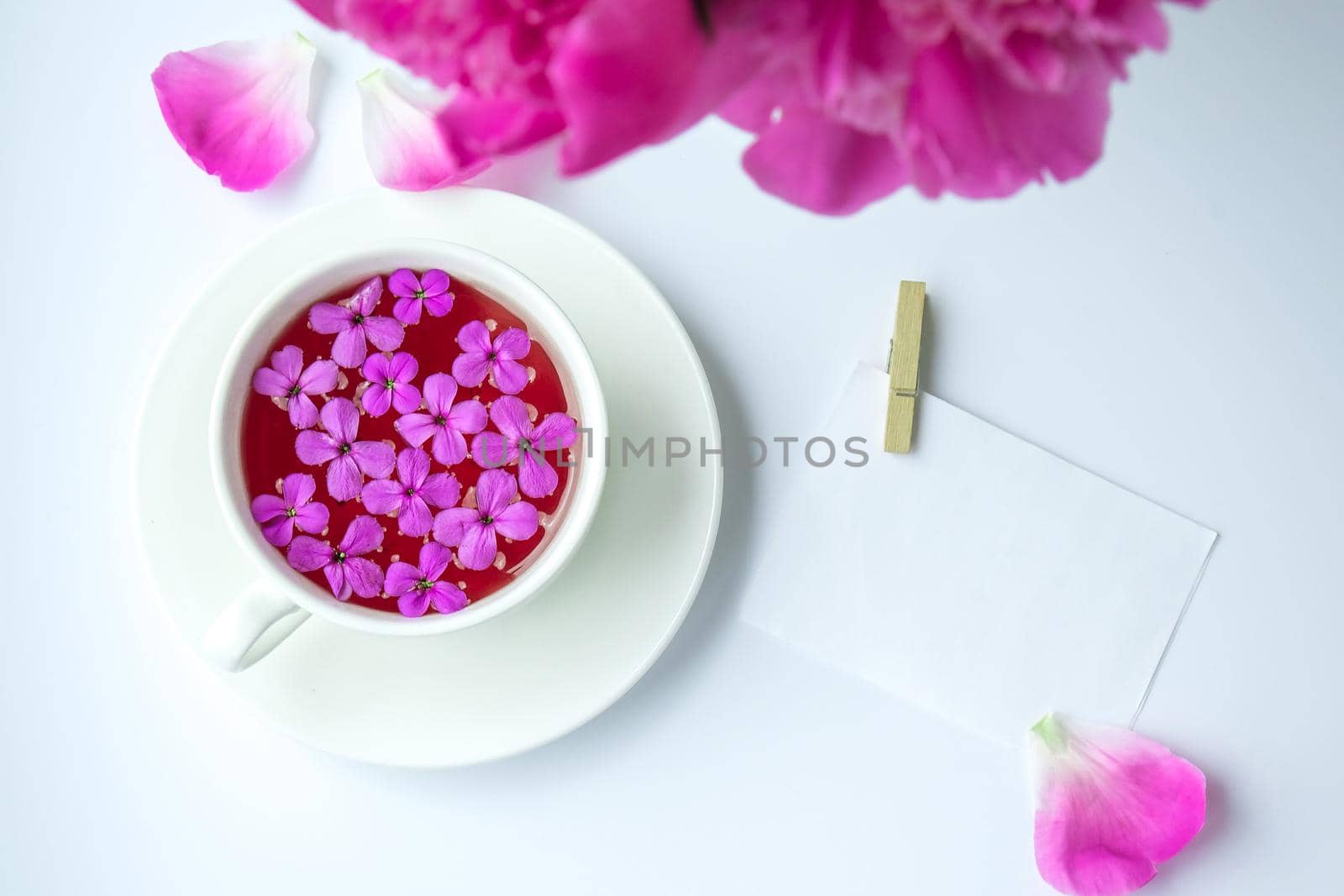 Creative layout with pink peonies flowers and cup of tea on bright table. Paper note. Copy space. Spring Seasonal valentine, woman, mother, 8 march holiday, romance breakfast. Stylish blogger. Greeting card. Invitation. Blog post