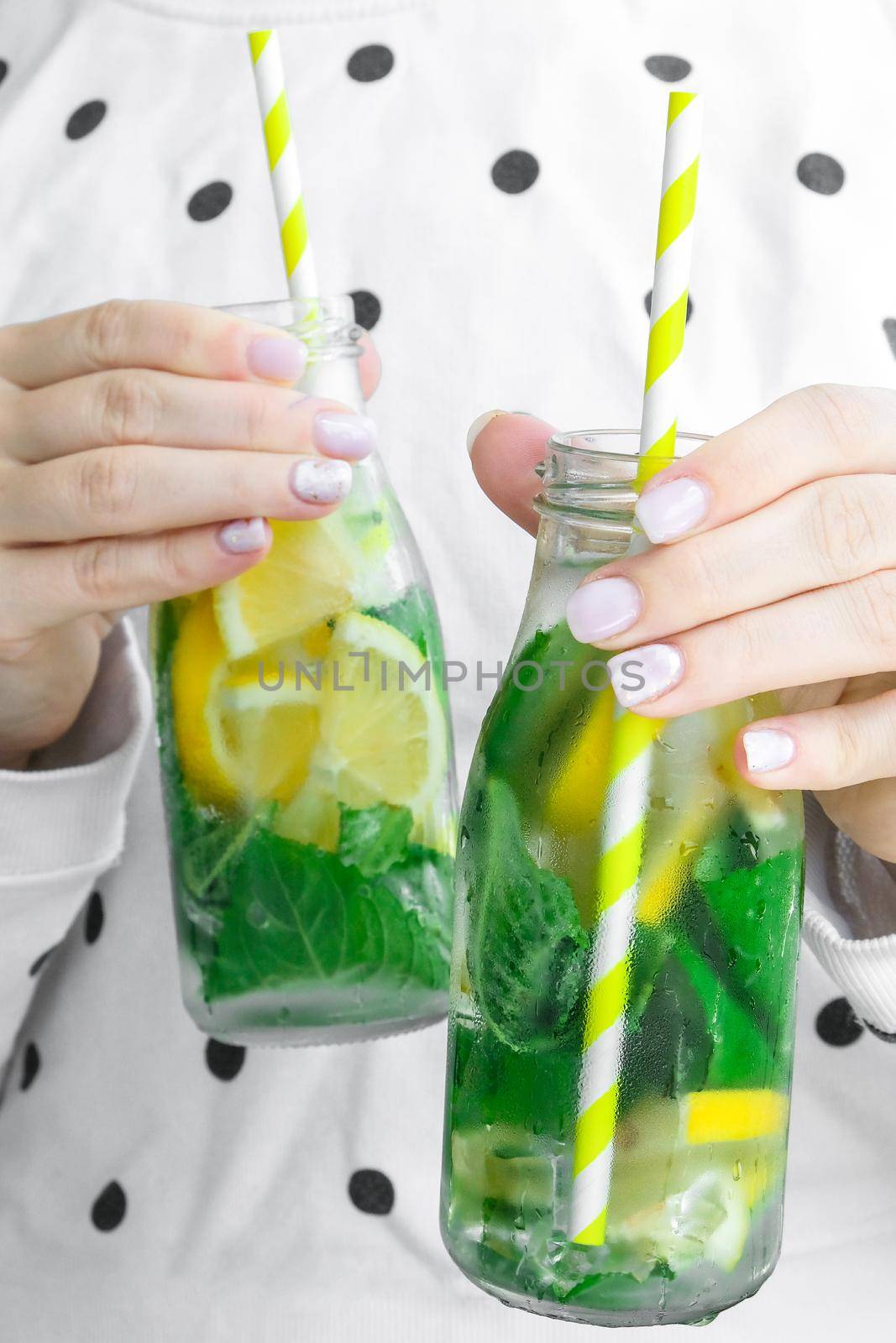 Female hand holding Mojito refreshing cocktail with eco paper drinking straw, alcohol drink. Lemonade with lemon and mint leaves. Summer refreshing detox drinks. Clean eating, healthy lifestyle concept, Diet. Nutrition.