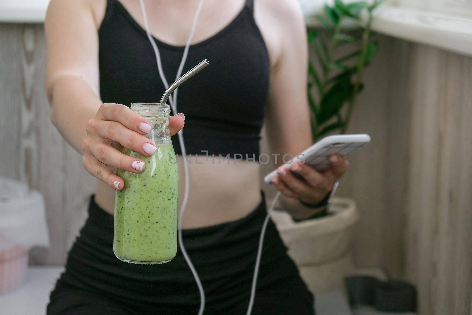 Young millenial woman checking smartphone drinking vegan smoothie drink detox. Woman doing yoga exercises at home. Online tuition Clean eating, weight loss, healthy dieting food concept. Stay healthy. Wellness