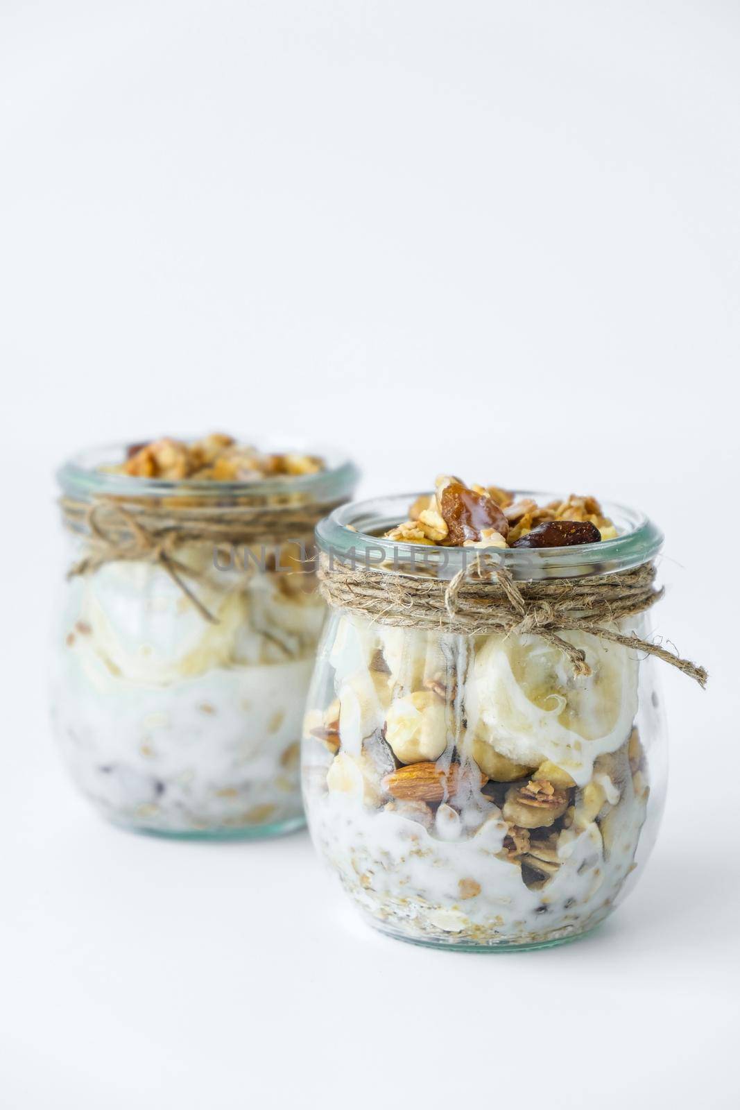 Healthy breakfast. Oatmeal Granola with greek yogurt and nuts banana muesli in jars on light background. Vegan, vegetarian and weight loss diet concept. Detox menu. Healthy eating food