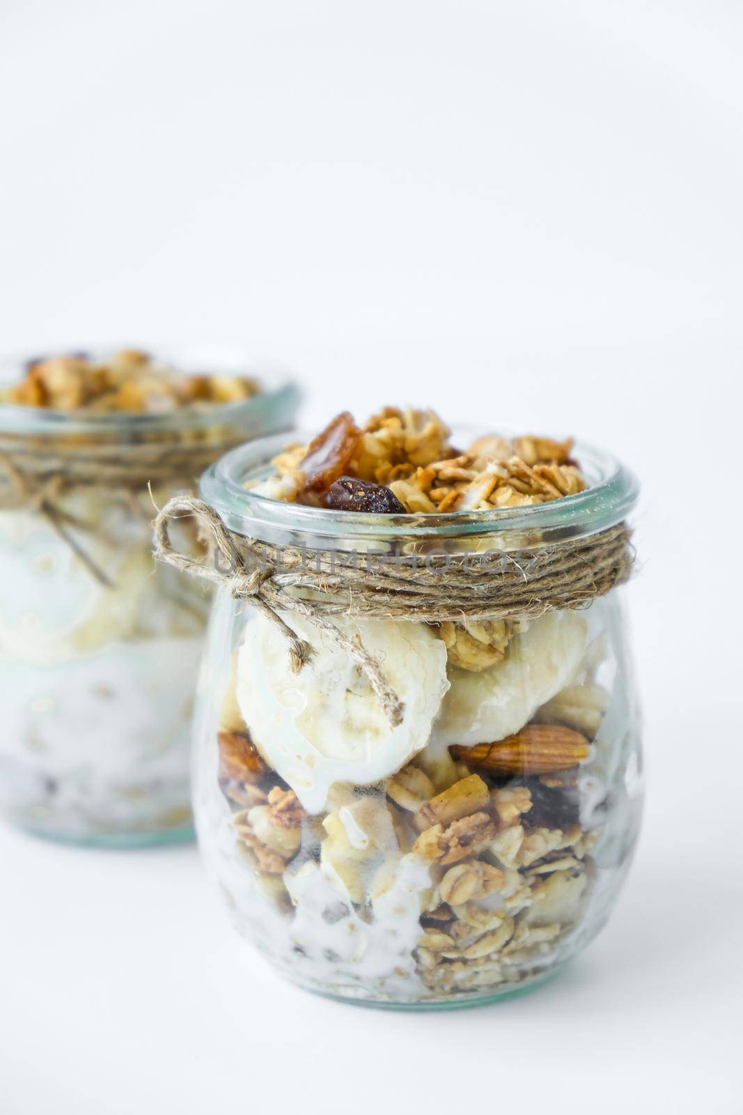 Healthy breakfast. Oatmeal Granola with greek yogurt and nuts banana muesli in jars on light background. Vegan, vegetarian and weight loss diet concept. Detox menu. Healthy eating food