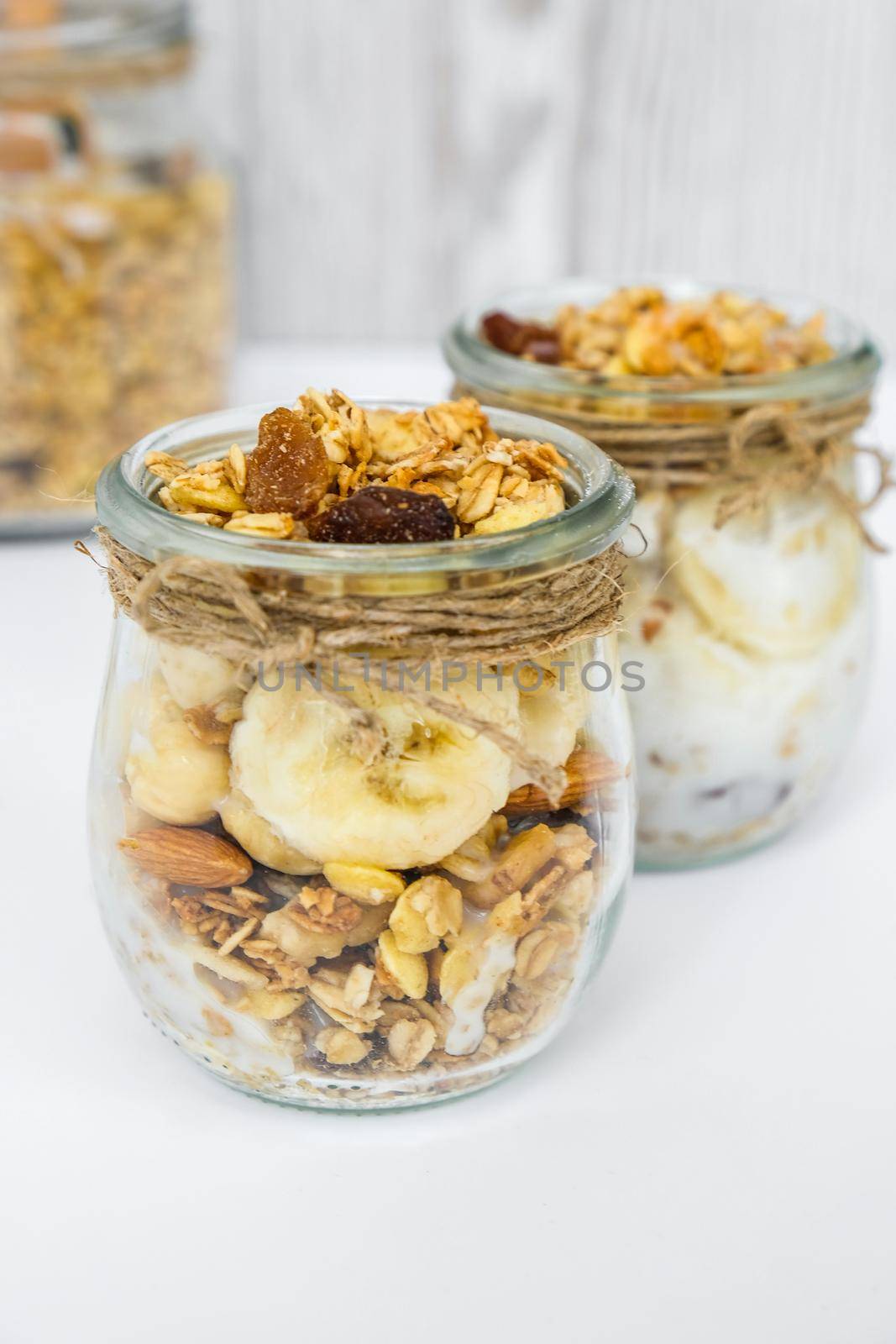 Healthy breakfast. Oatmeal Granola with greek yogurt and nuts banana muesli in jars on light background. Vegan, vegetarian and weight loss diet concept. Detox menu. Healthy eating food