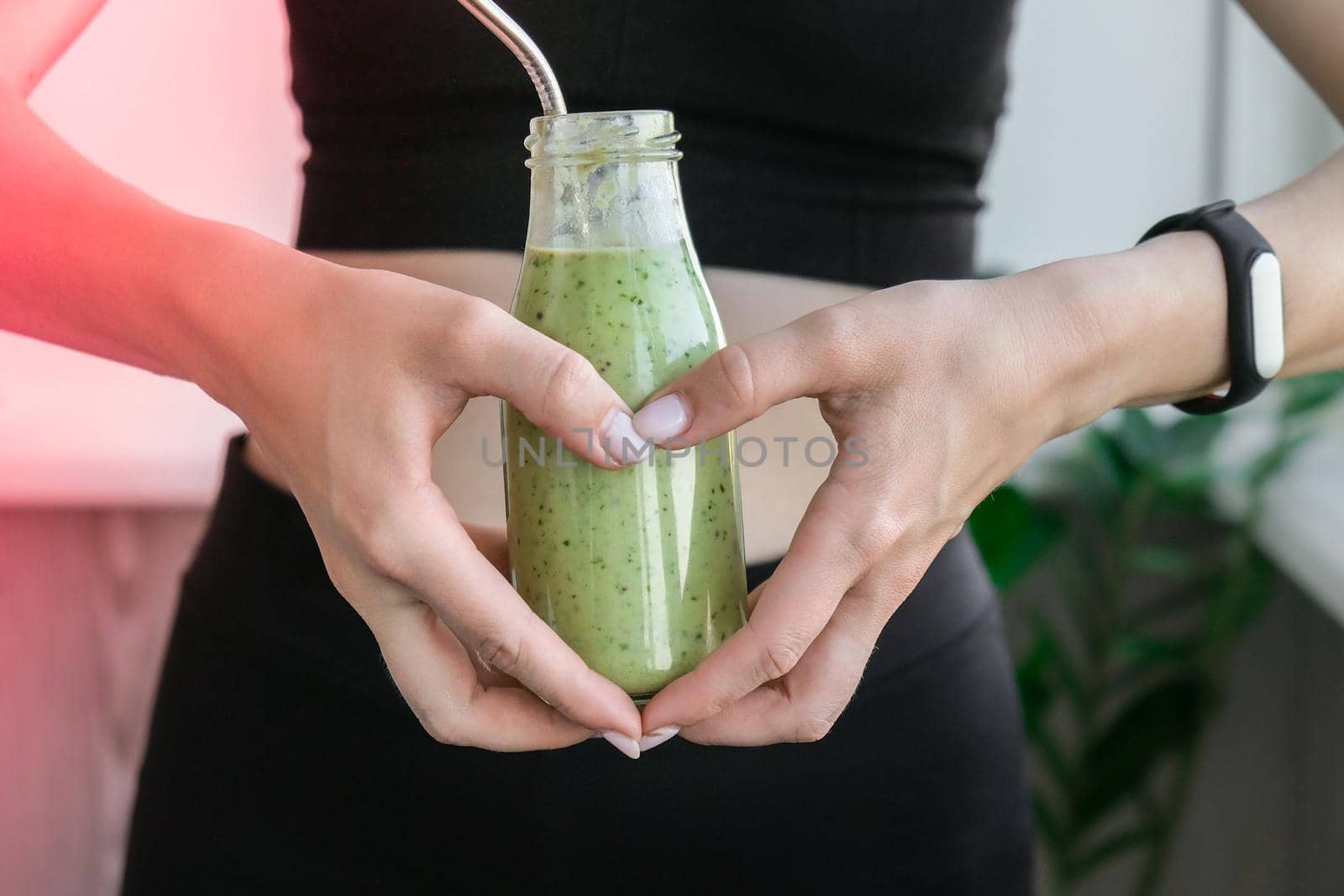Hand in heart symbol holding smoothie drink detox on fit and slim belly woman. Fitness wellbeing concept. Body care, clean eating, weight loss diet concept. Woman with bowel or reproductive problem. Working out at home. Belly waist exercises