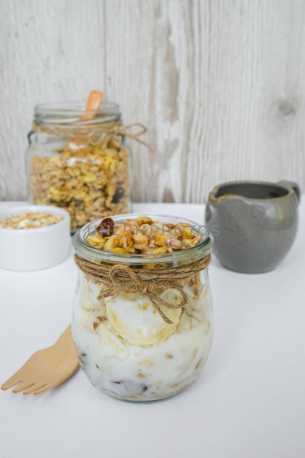 Healthy breakfast. Oatmeal Granola with greek yogurt and nuts banana muesli in jars on light background. Vegan, vegetarian and weight loss diet concept. Detox menu. Healthy eating food