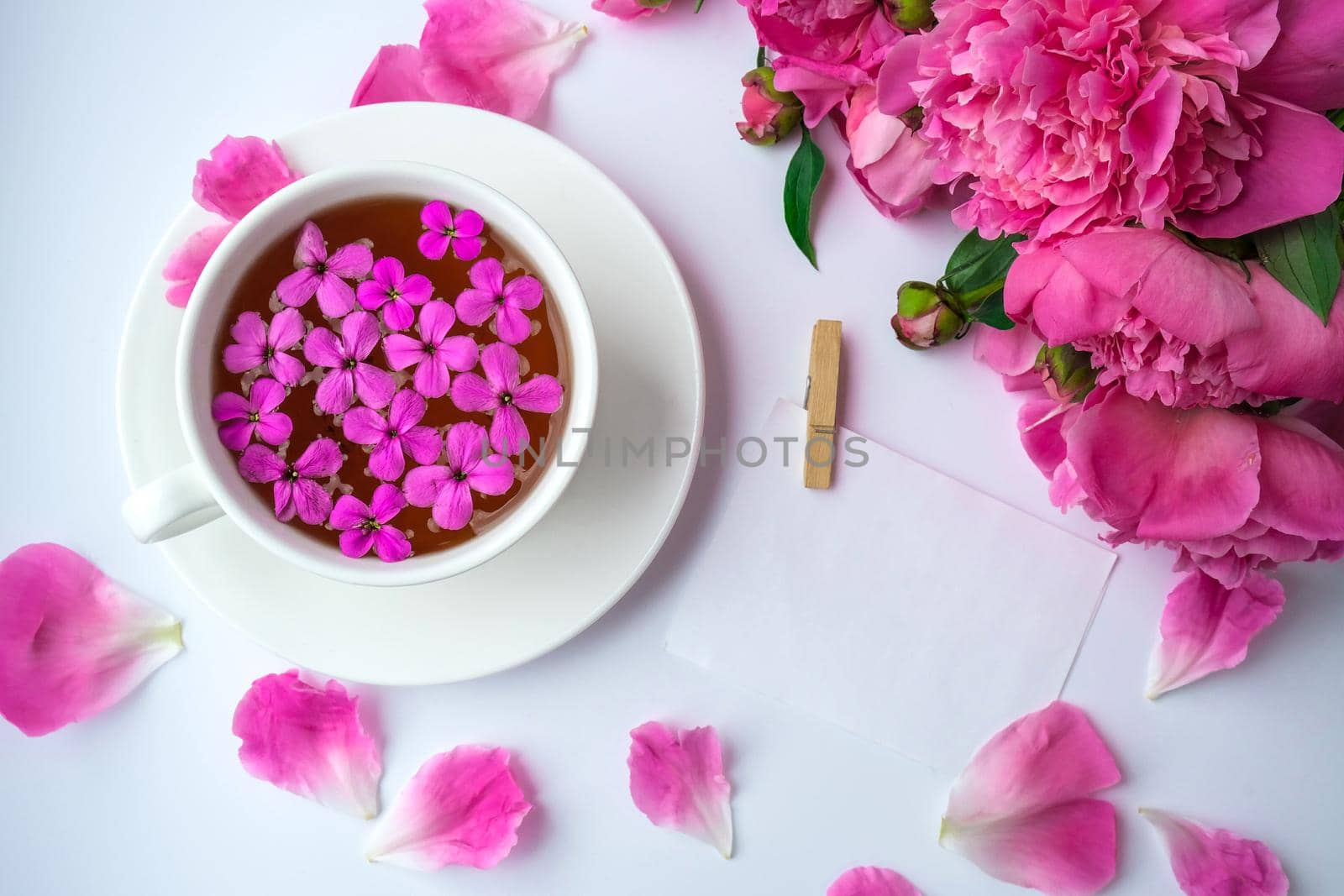 Creative layout with pink peonies flowers and cup of tea on bright table. Paper note. Copy space. Spring Seasonal valentine, woman, mother, 8 march holiday, romance breakfast. Stylish blogger. Greeting card. Invitation. Blog post