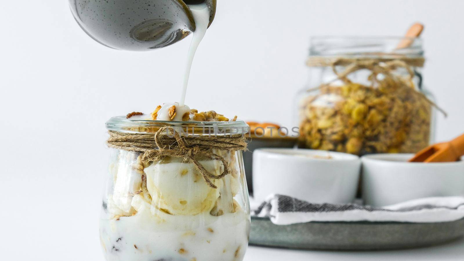 Healthy breakfast. Oatmeal Granola with greek yogurt pouring and nuts banana muesli in jars on light background. Vegan, vegetarian and weight loss diet concept. Detox menu. Healthy eating food