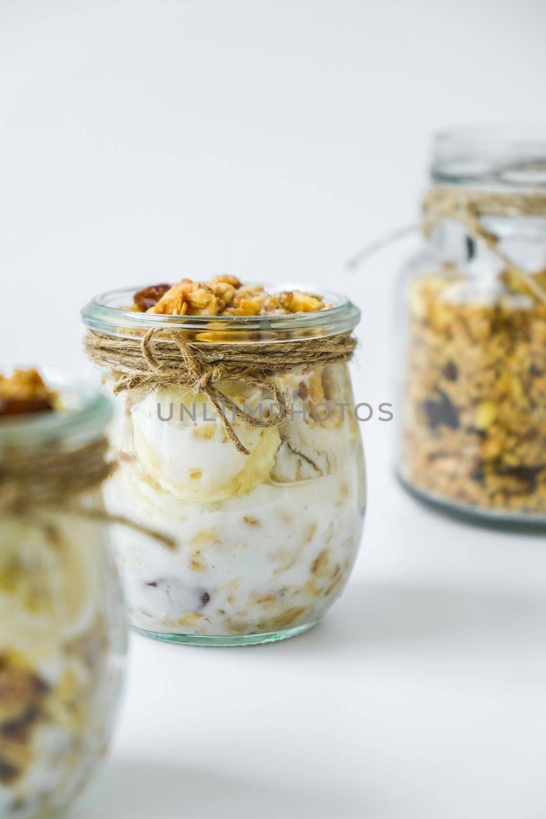 Healthy breakfast. Oatmeal Granola with greek yogurt and nuts banana muesli in jars on light background. Vegan, vegetarian and weight loss diet concept. Detox menu. Healthy eating food