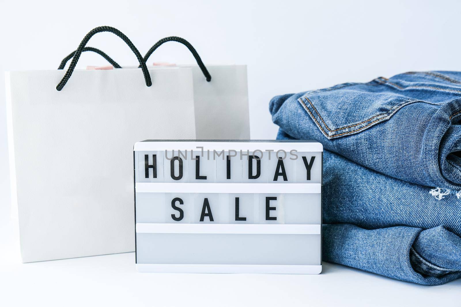 Light board with text HOLIDAY SALE with paper shopping bags, jeans clothes. Big Sale online shopping concept. Promotion advertising. Holiday Cyber monday.