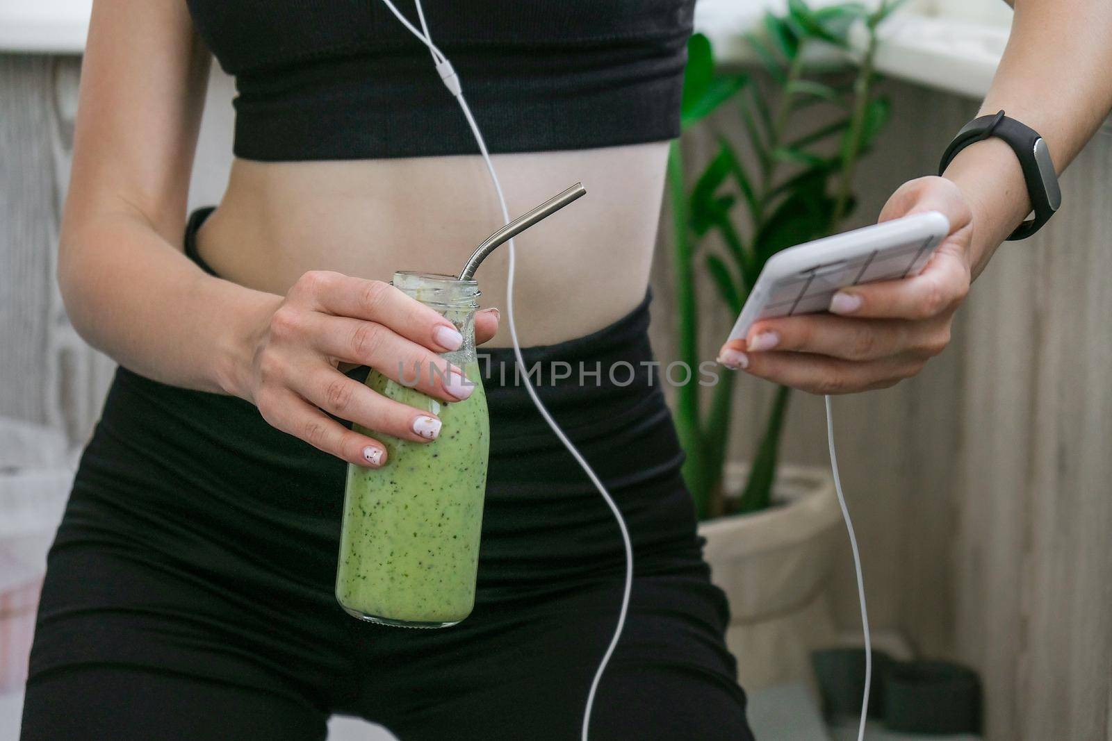 Young millenial woman checking smartphone drinking vegan smoothie drink detox. Woman doing yoga exercises at home. Online tuition Clean eating, weight loss, healthy dieting food concept. Stay healthy. Wellness