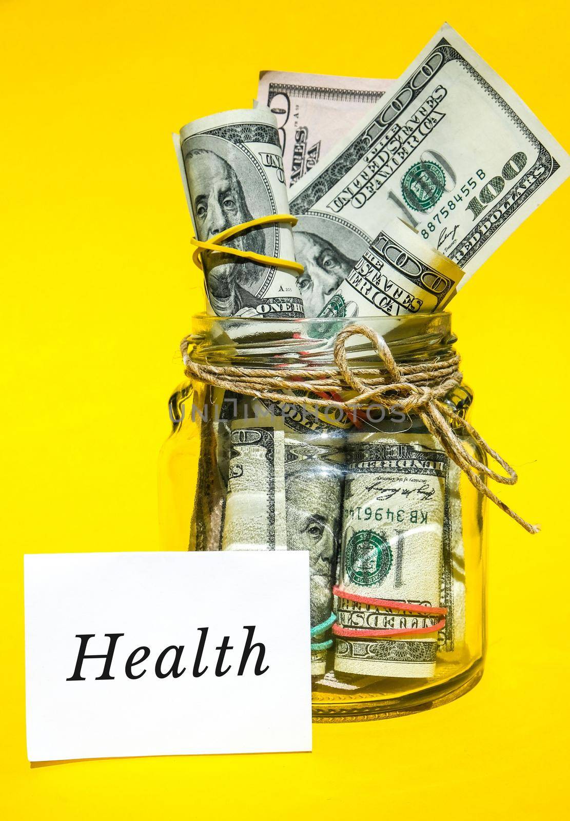 Glass jars filled with dollar bills, savings inside glass jar, money isolated on yellow background. Paper note written word HEALTH. Business budget of wealth and prosperity finance