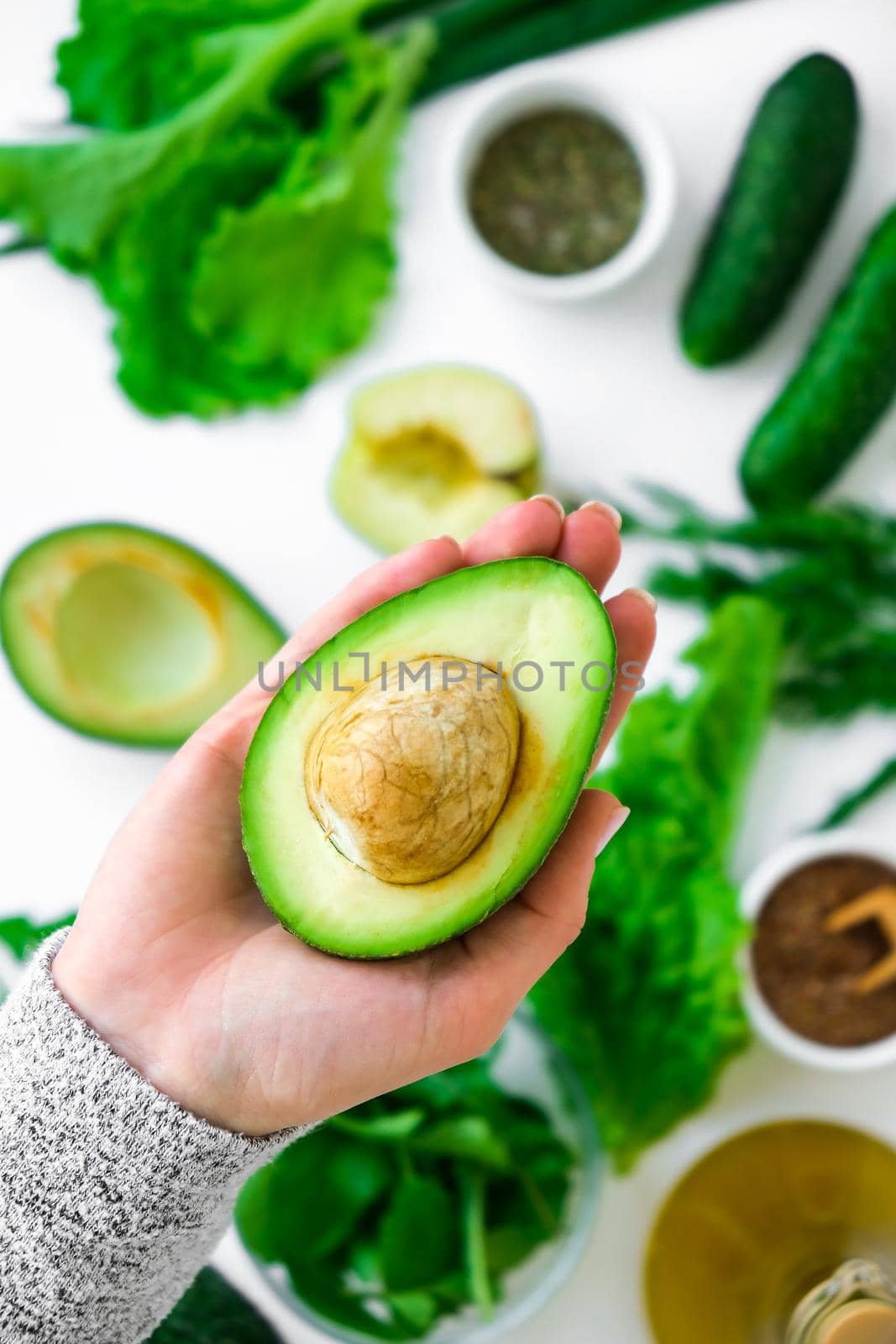 Woman cooking salad of fresh green vegetables and herbs. Cooking healthy diet or vegetarian food. Female hands hold avocado surrounded by green vegetables. Step by step recipe. Healthy eating. Ingredients for salad. Pattern flat lay with healthy vegetarian meal ingredients. Raw food concept. A variety of organic fruits and vegetables with avocado. Vegan menu. Fresh spinach and green onion leaves.