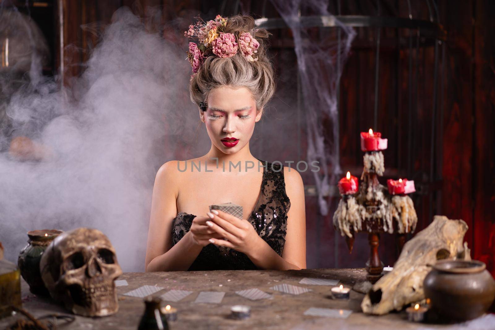 Portrait fortune teller woman reading future on magical cards. Magic and divination. Young beautiful enchanted female witch sitting on the table waiting your desire. Scary Halloween atmosphere