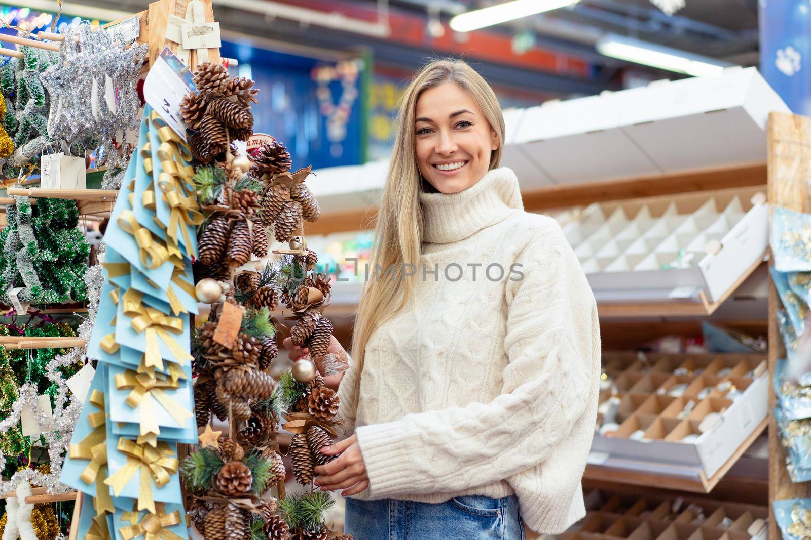 Christmas decoration shopping. Caucasian woman choose new year decor in shopping mall. Medium age female dressed white sweater buying christmas ornament toys indoor store