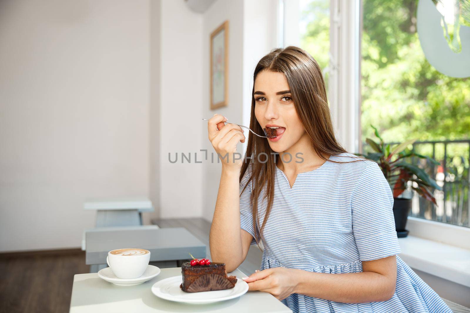 Young attractive Caucasian lady enjoy eating chocolate cake with hot coffee in modern coffee shop at noon. by Benzoix