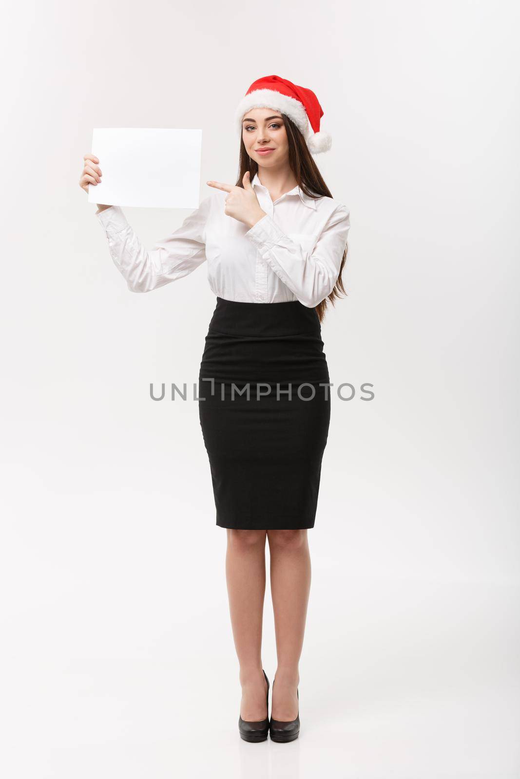 Business Concept - Beautiful young caucasian business woman with santa hat pointing to blank paper using for advertising. by Benzoix