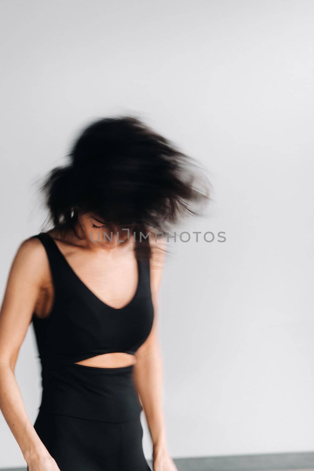 A blurry silhouette of a woman in black sportswear is engaged in dynamic kali meditation in the yoga hall.