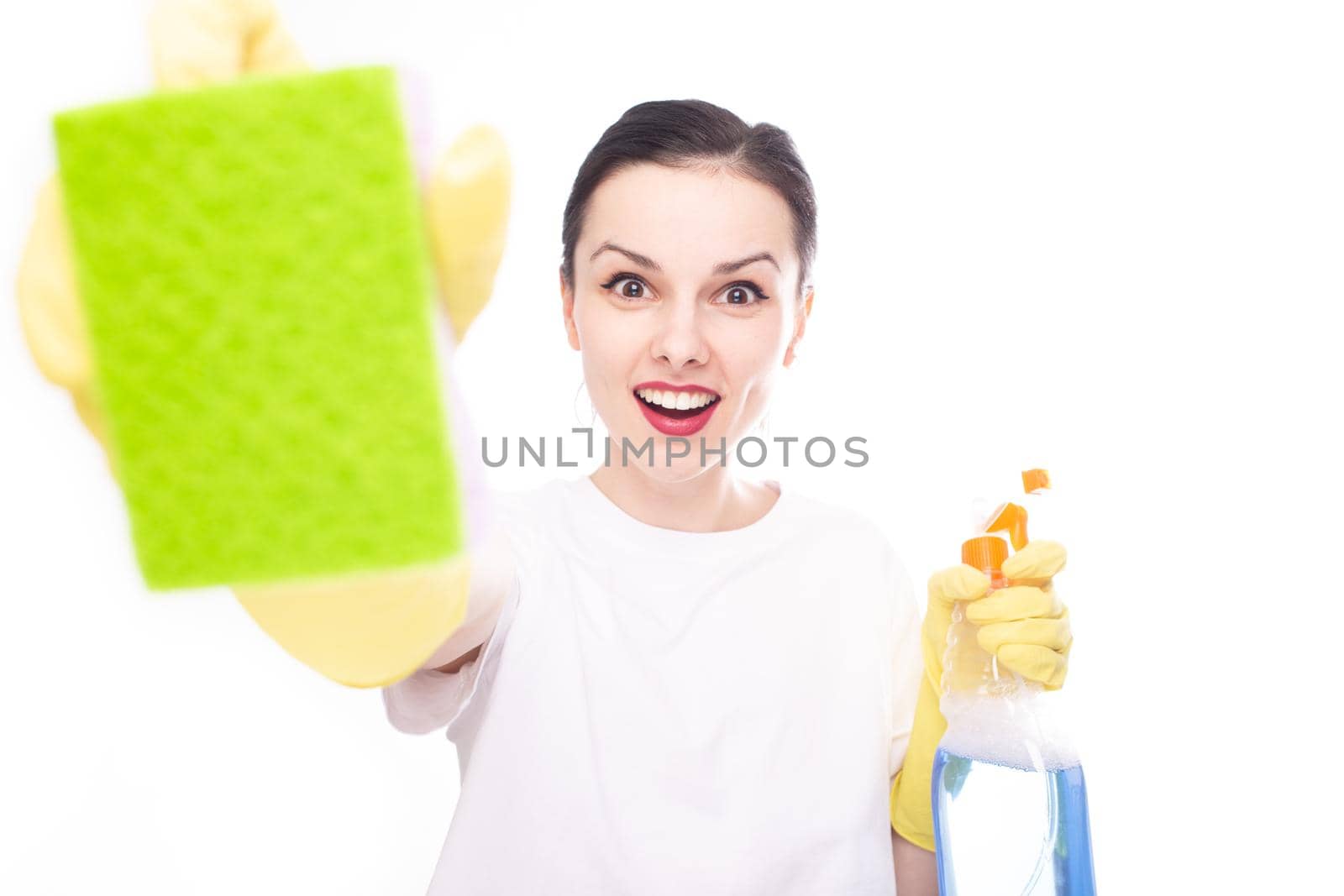 happy woman in yellow gloves shows a green sponge in her other hand she has a cleaning product, white studio background. High quality photo