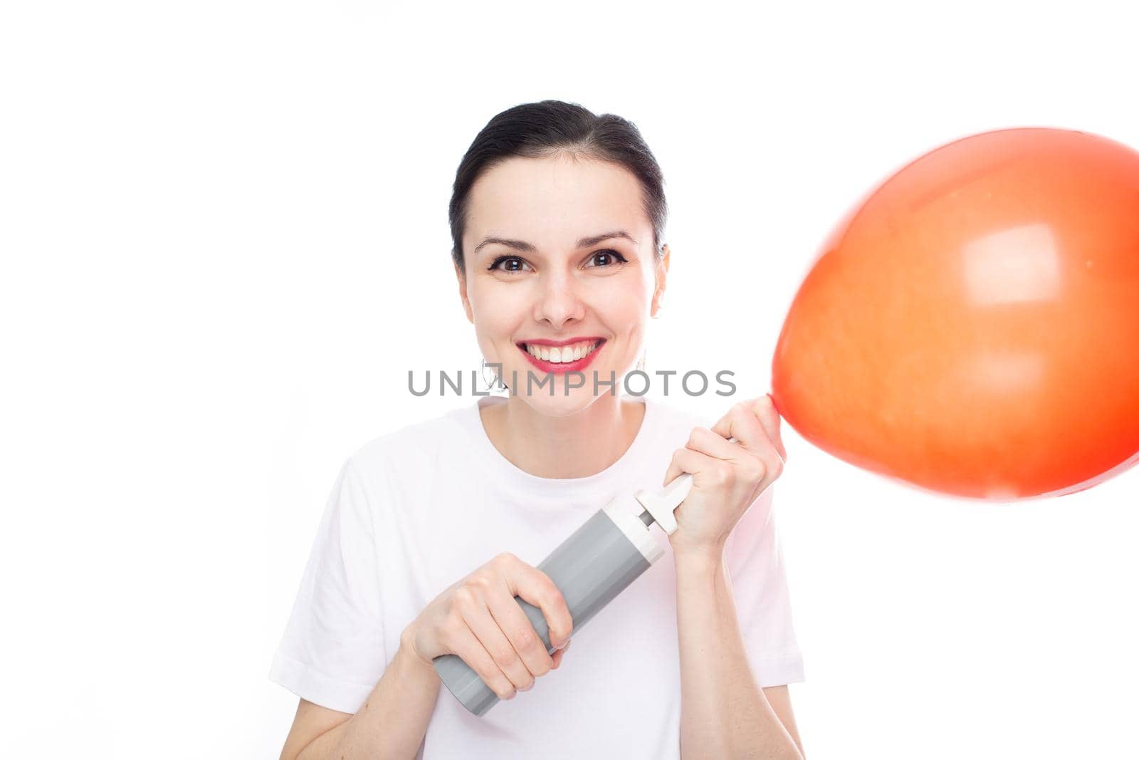 happy woman in white t-shirt inflates red balloon, white studio background. High quality photo