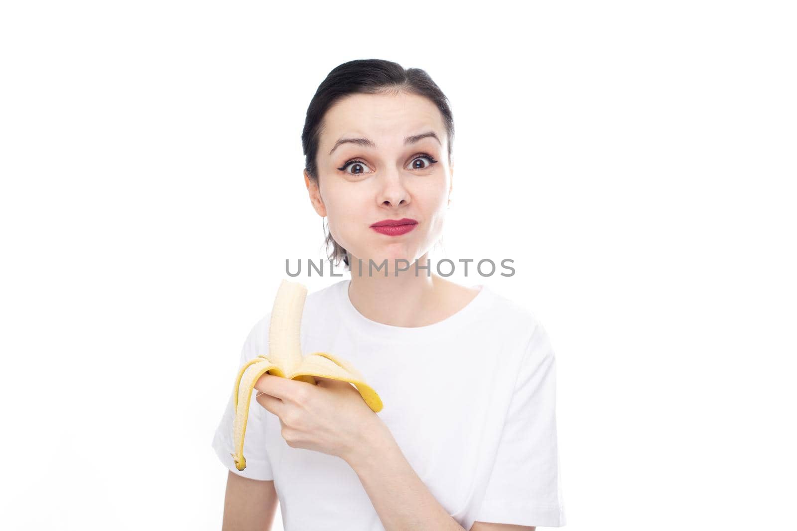 funny woman in white t-shirt eating banana, white studio background. High quality photo
