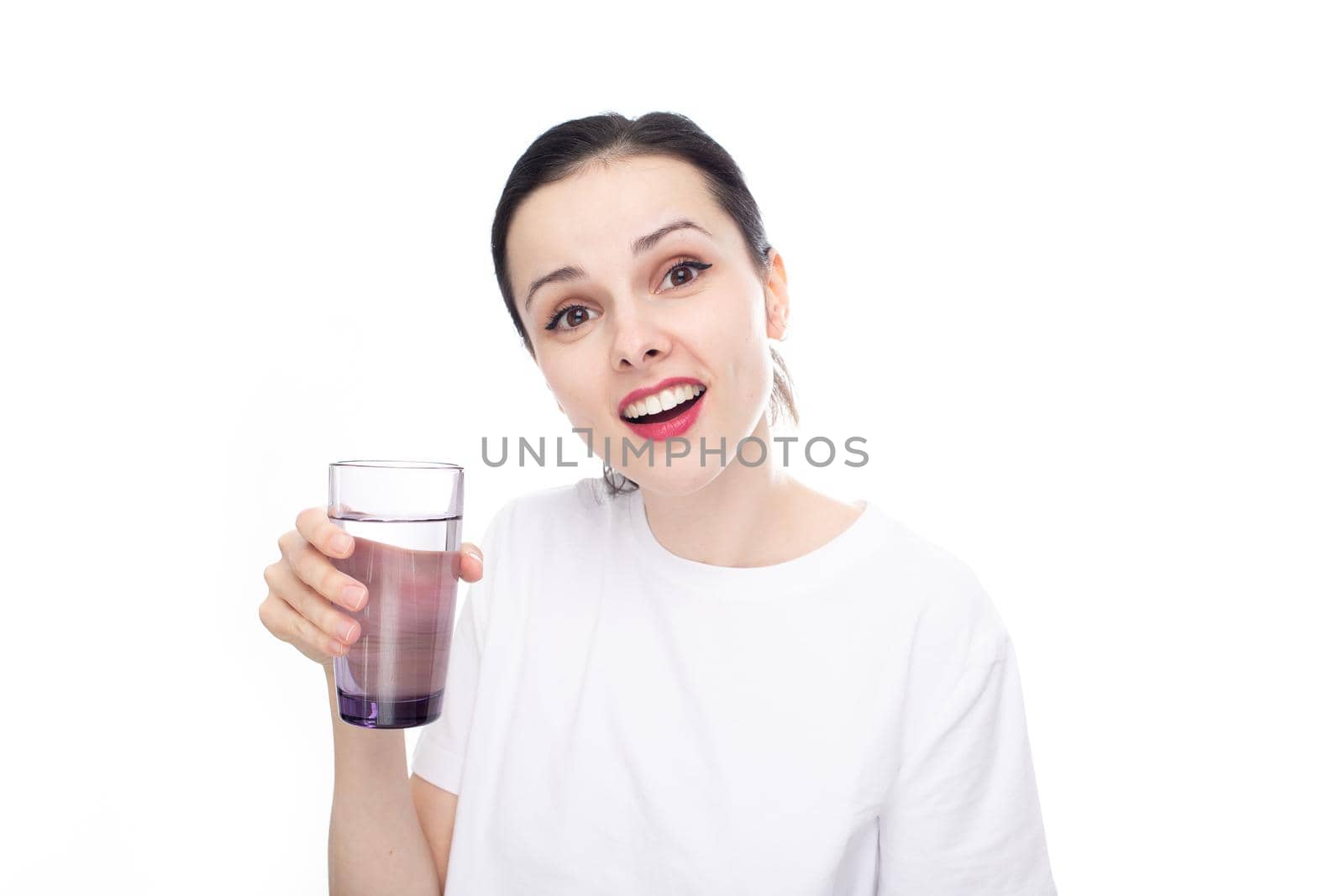 smiling woman in a white t-shirt holds a glass of water in her hand, white studio background. High quality photo