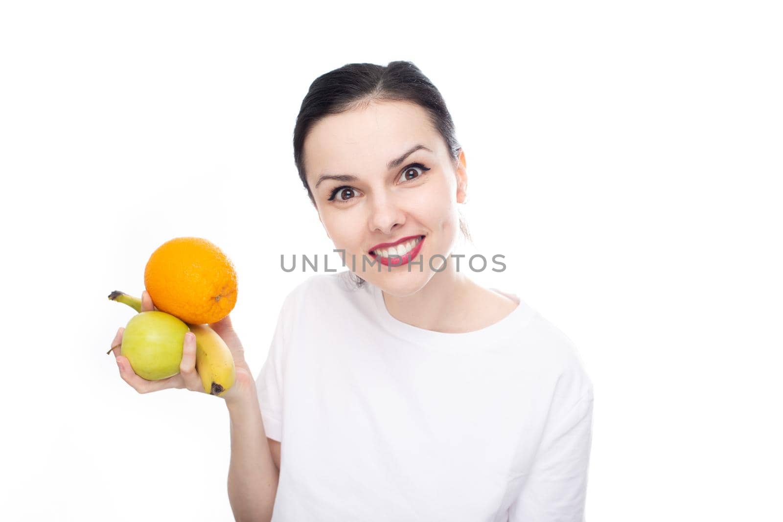 smiling woman in white t-shirt holding apple orange and banana in her hand, white background. High quality photo