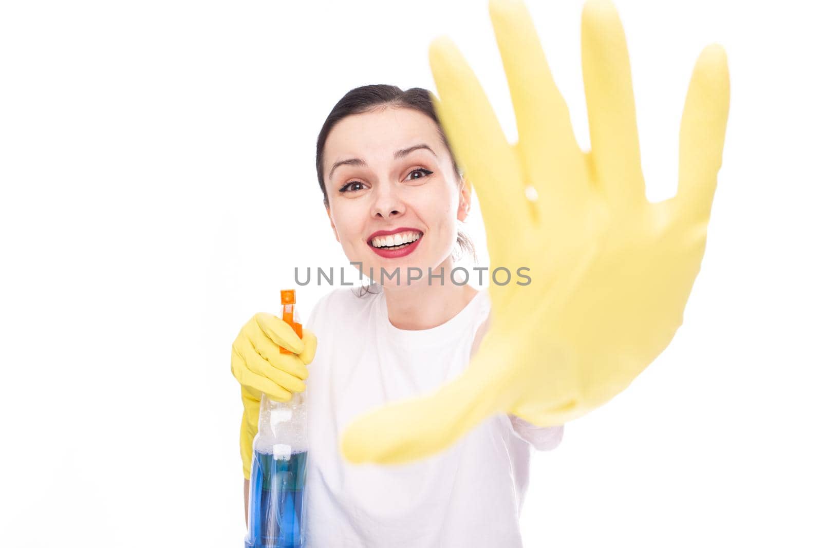 happy female cleaner in yellow gloves for cleaning shows with her hand a stop sign, in her other hand she has window cleaner, white studio background. High quality photo