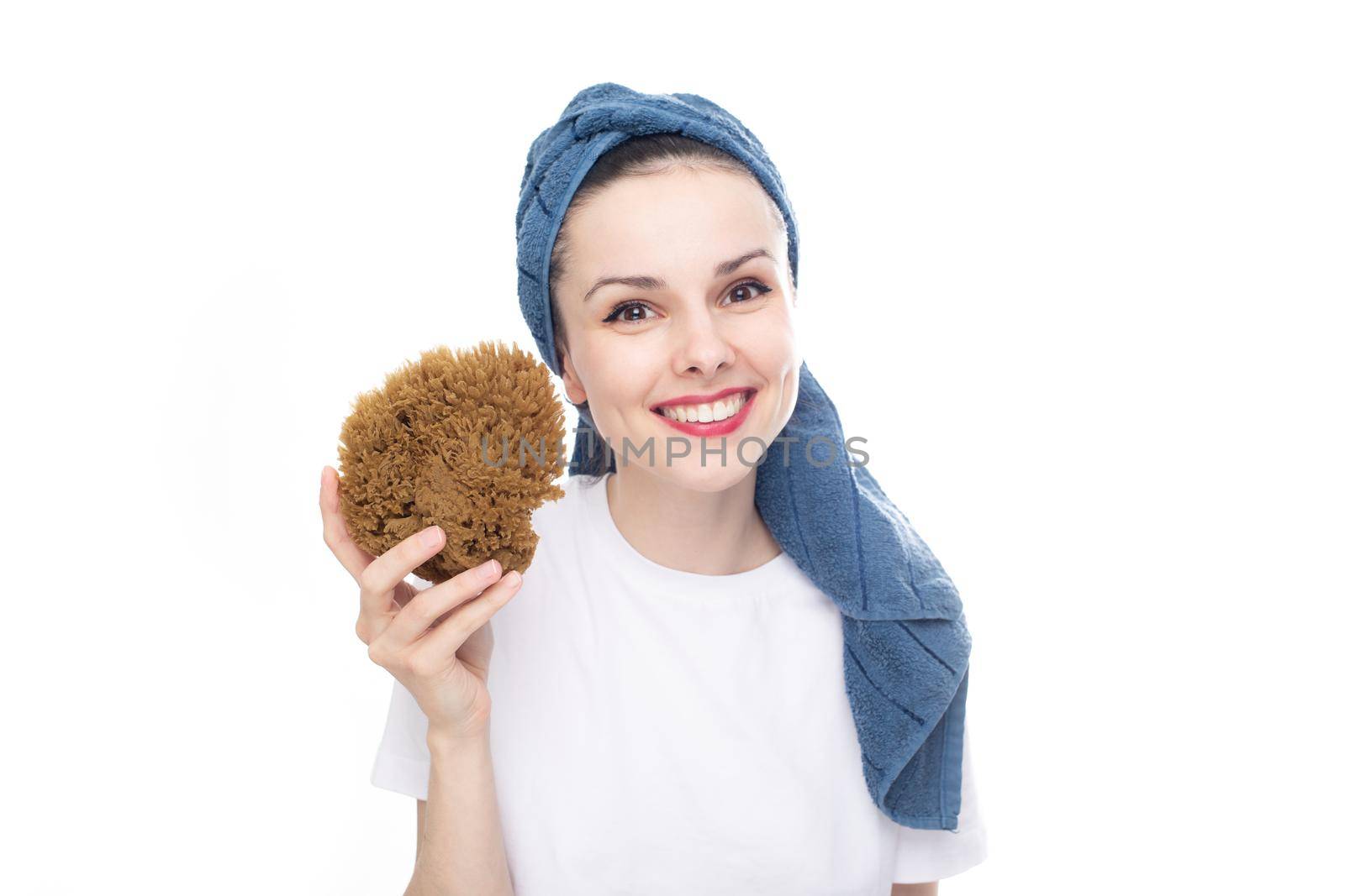smiling woman in a white t-shirt and a blue towel on her head holds a body washcloth made of natural seaweed in her hand, white studio background. High quality photo