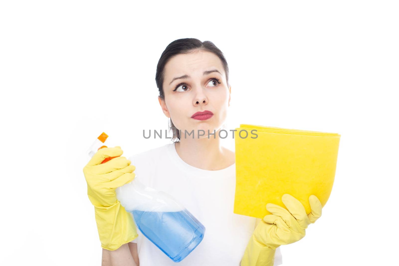 pensive woman in a white t-shirt on her hands yellow cleaning gloves holds window cleaner and rags in her hands, white background. High quality photo