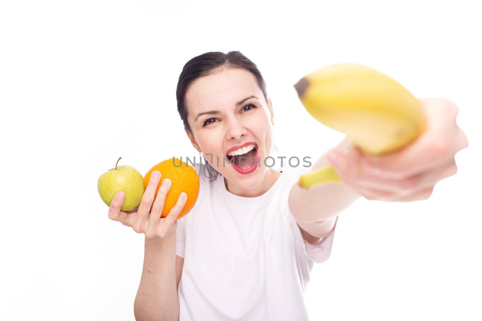 smiling woman in white t-shirt holding apple orange and banana in her hands, white background. High quality photo