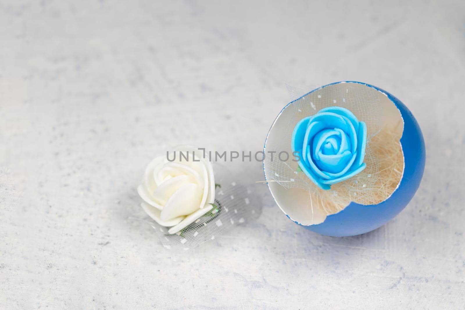 blue artificial rose inside a blue broken egg next to a fake white rose. Happy easter concept. soft focus