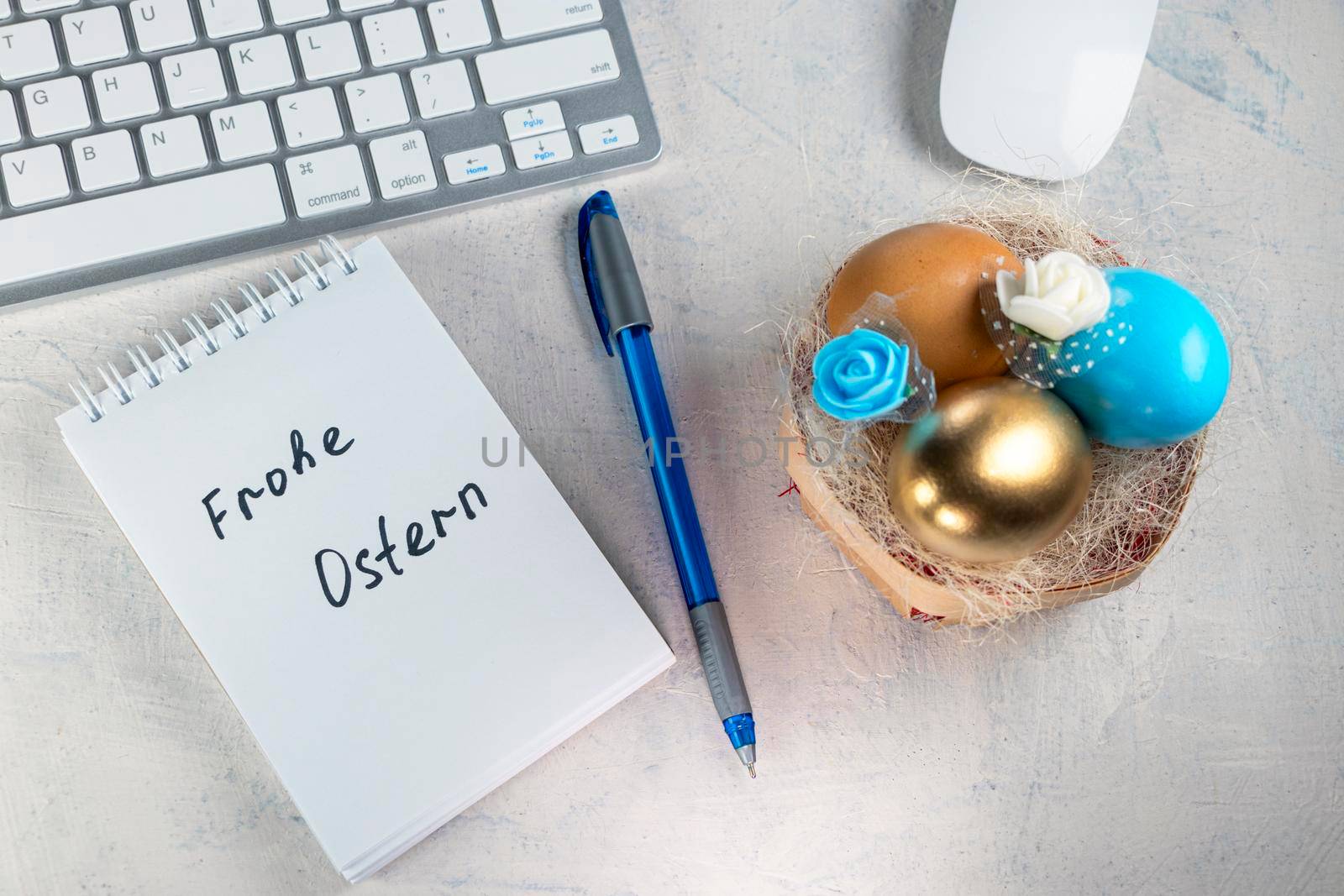 The words in German Frohe Ostern or Happy Easter in a notebook on the desktop with colored eggs in a nest and colored feathers. Easter in the office. by Leoschka