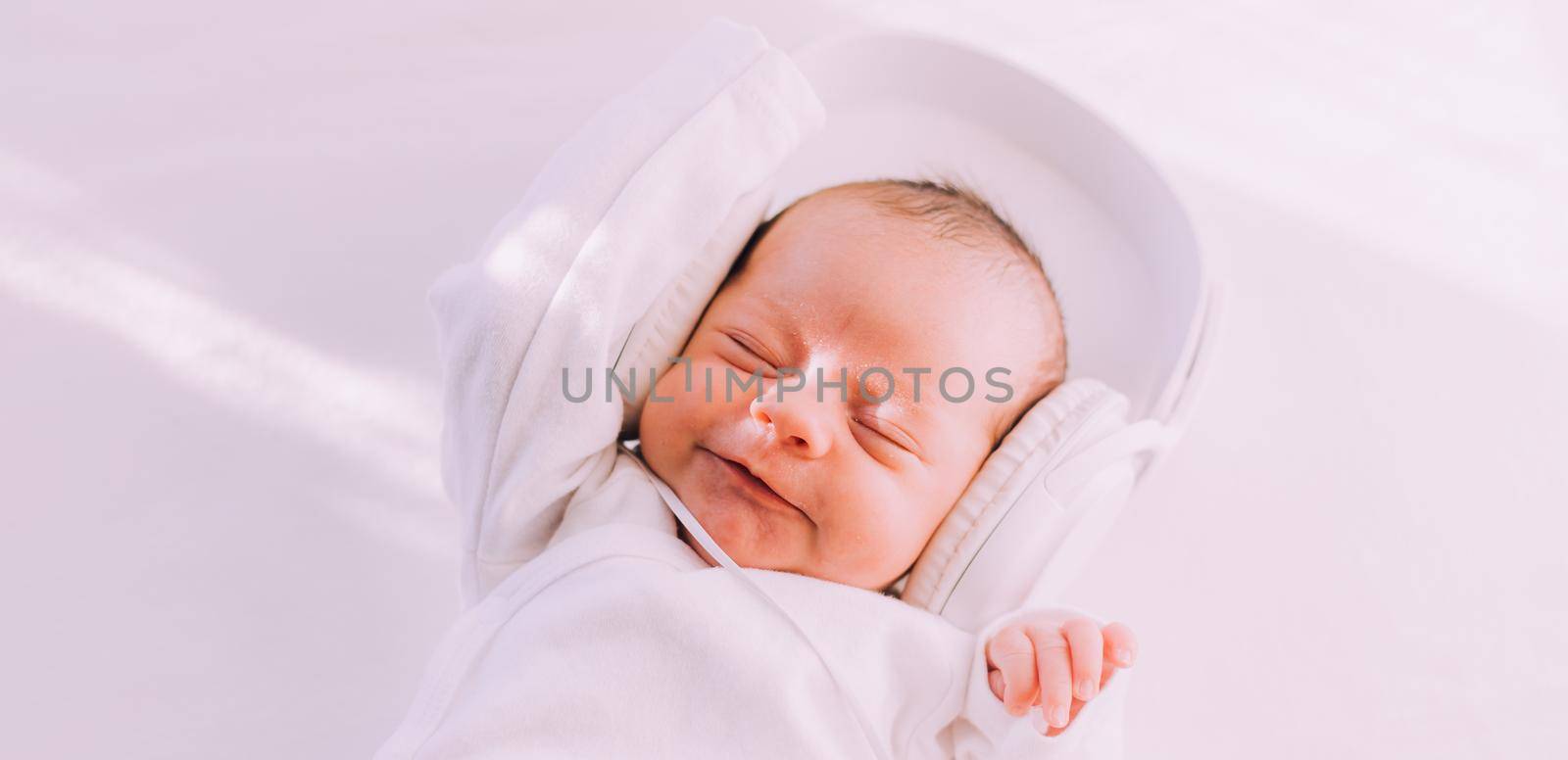 The kid is wearing headphones . Happy baby. A newborn baby. White on white