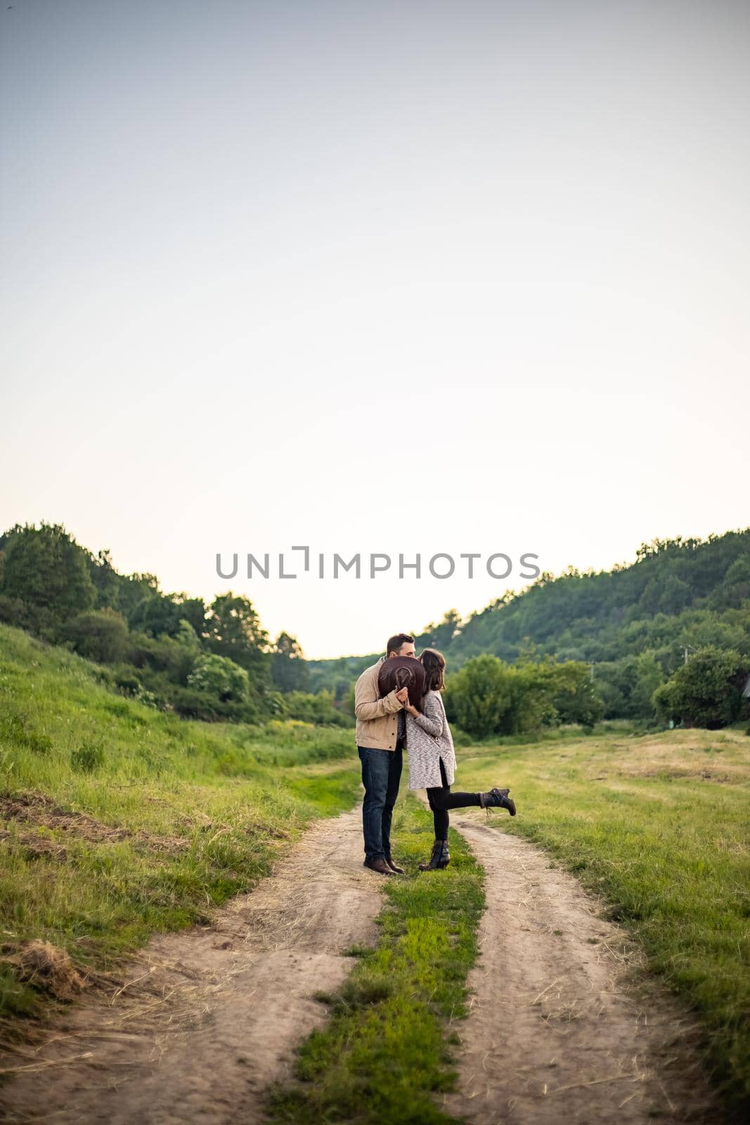 young couple on a village road kissing covered with a hat by Anyatachka