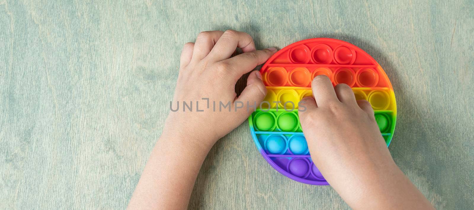 banner with Kid playing with pop it sensory toy. boy pressing on colorful rainbow squishy soft silicone bubbles. Stress and anxiety relief. Trendy fidgeting game by Leoschka
